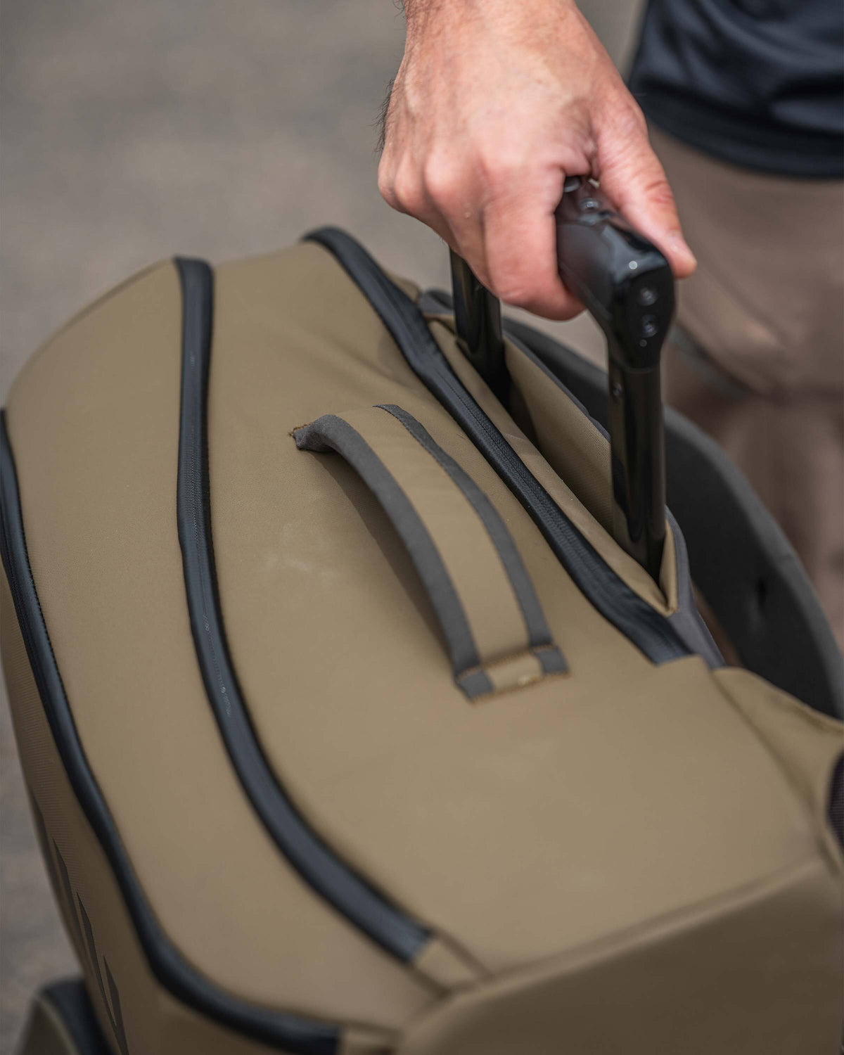 Person showcasing the luggage handle sleeve on the Waypoint Travel Backpack, located behind the back panel for securing over roller luggage handle.