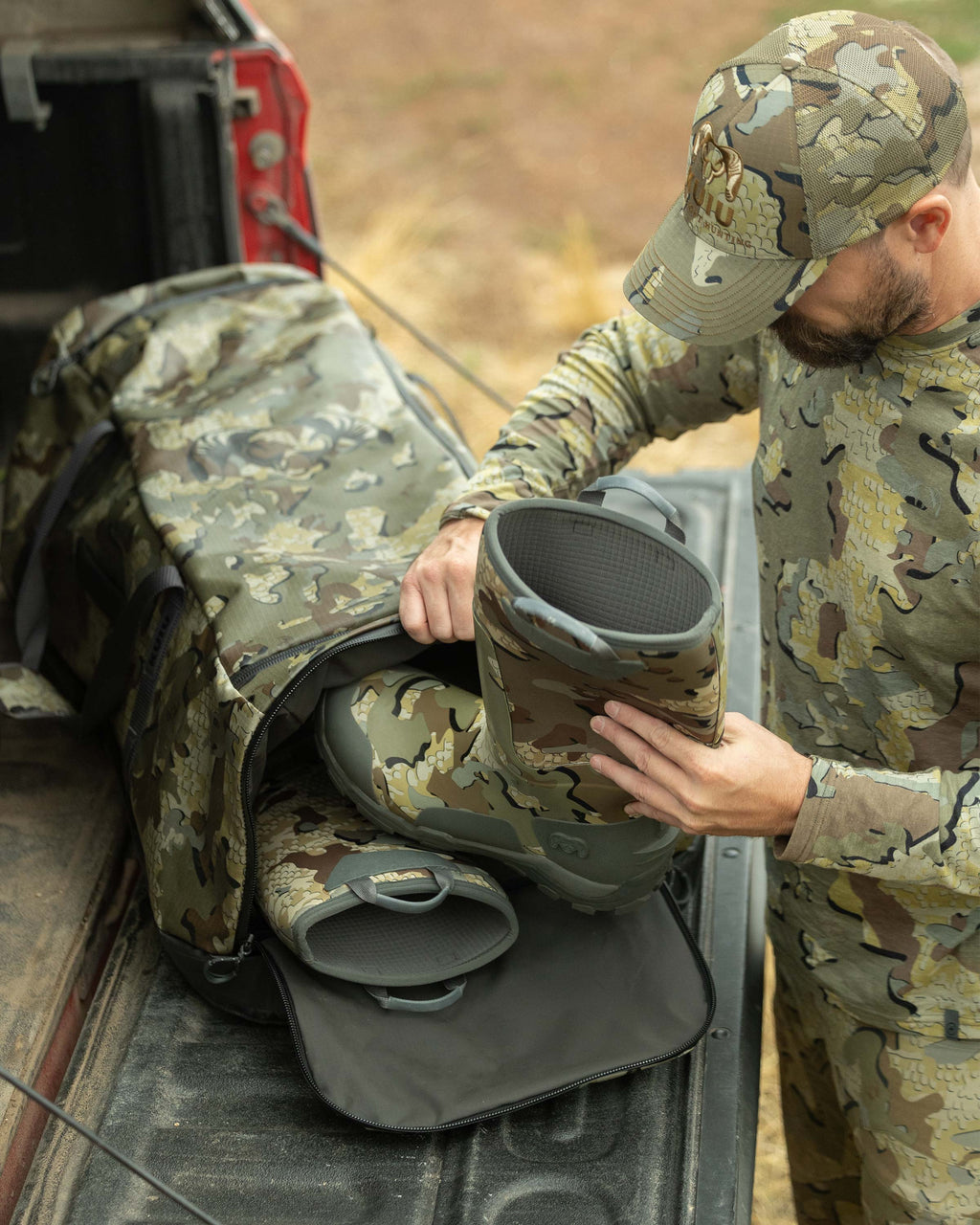 Hunter putting his KUIU HD Mud Boot in the end pocket of the TwoTrack 8000 Boot Duffel in Valo Camouflage