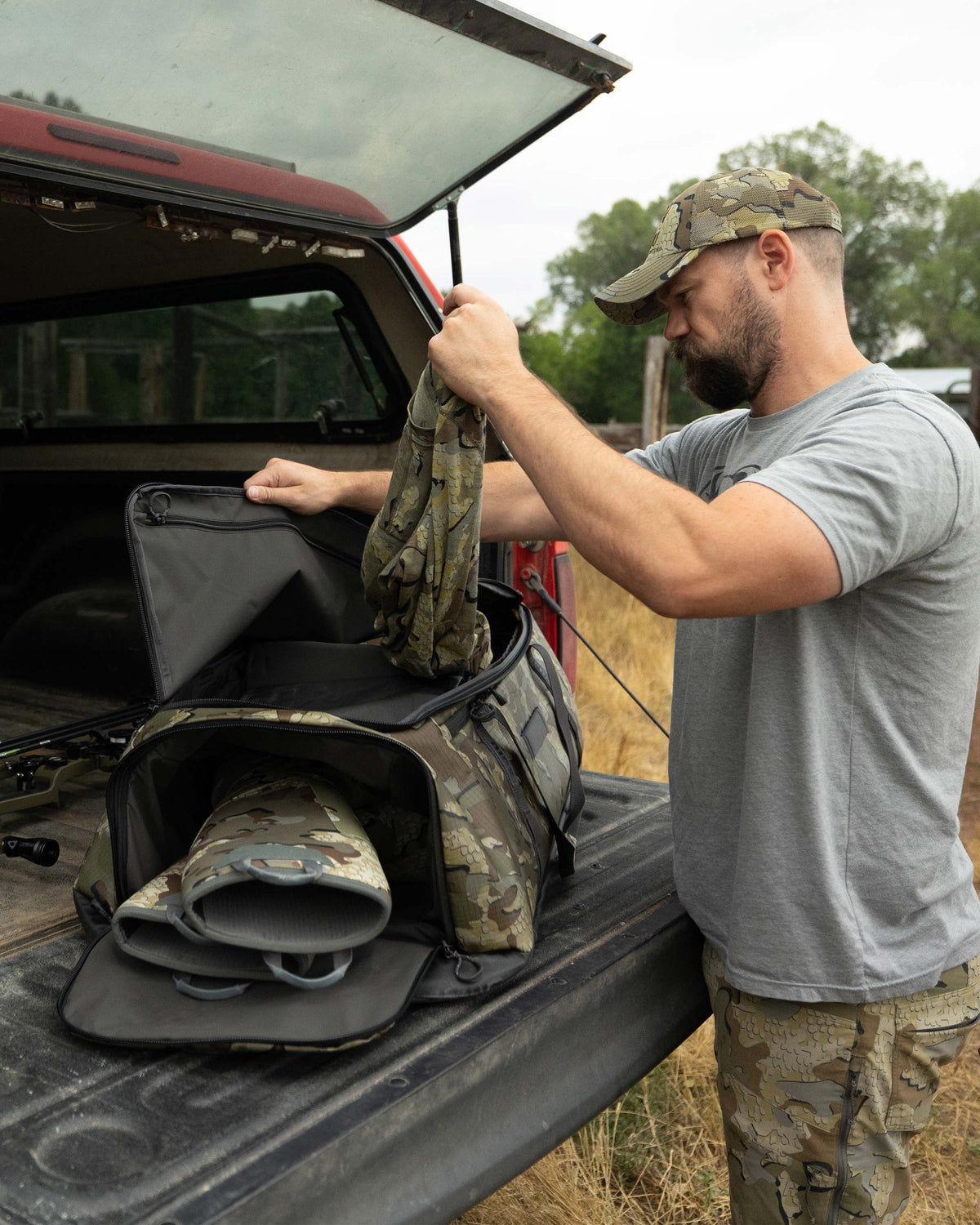 Hunter stands behind his truck tailgate, unpacking clothes from the TwoTrack 8000 Duffel in Valo Camouflage