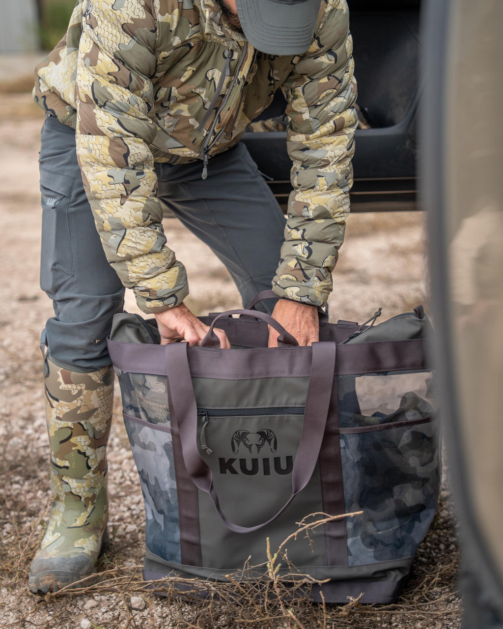 Hunter slightly bent over unzipping KUIU 3500 Mesh Tote Bag in Vias Storm