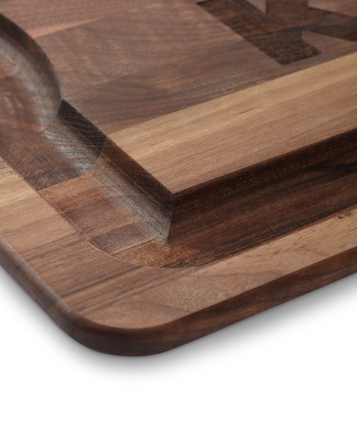 Close-up of a KUIU Engraved Walnut Cutting Board with a carved recessed bowl and rounded corners, showing layered wood grain in warm brown and amber tones.