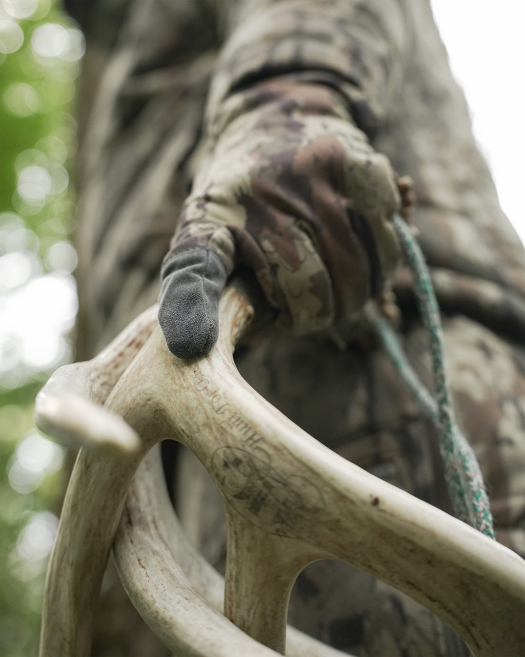 A close-up outdoor shot of a person in  holding a large antler wearing StrongFleece 290 Gloves in Veros Camouflage with a blurred natural background.