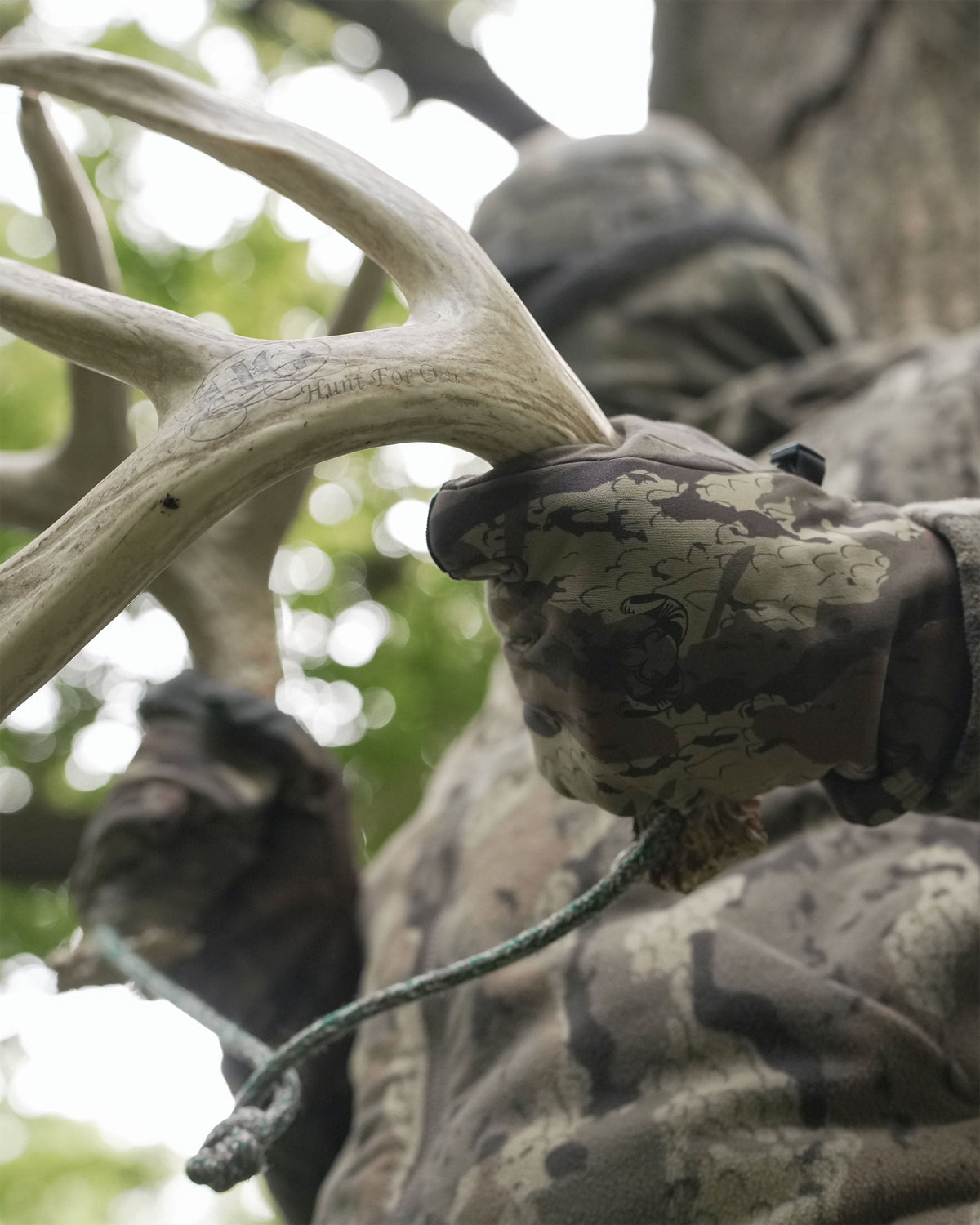 A close-up action shot of a hunter wearing StrongFleece 290 Gloves in Veros Camouflage holds and rattles two deer antlers together.