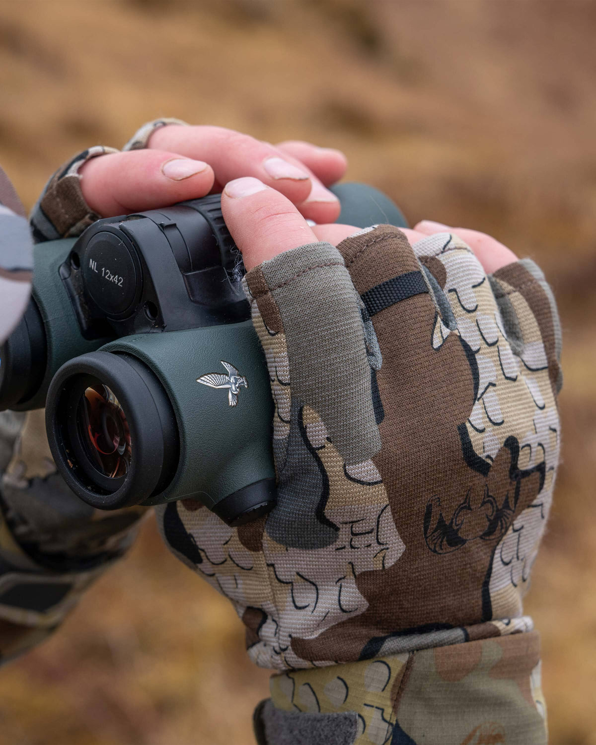 Hunter looking through a binocular, wearing ULTRA Merino Fingerless Glove in Valo Camouflage