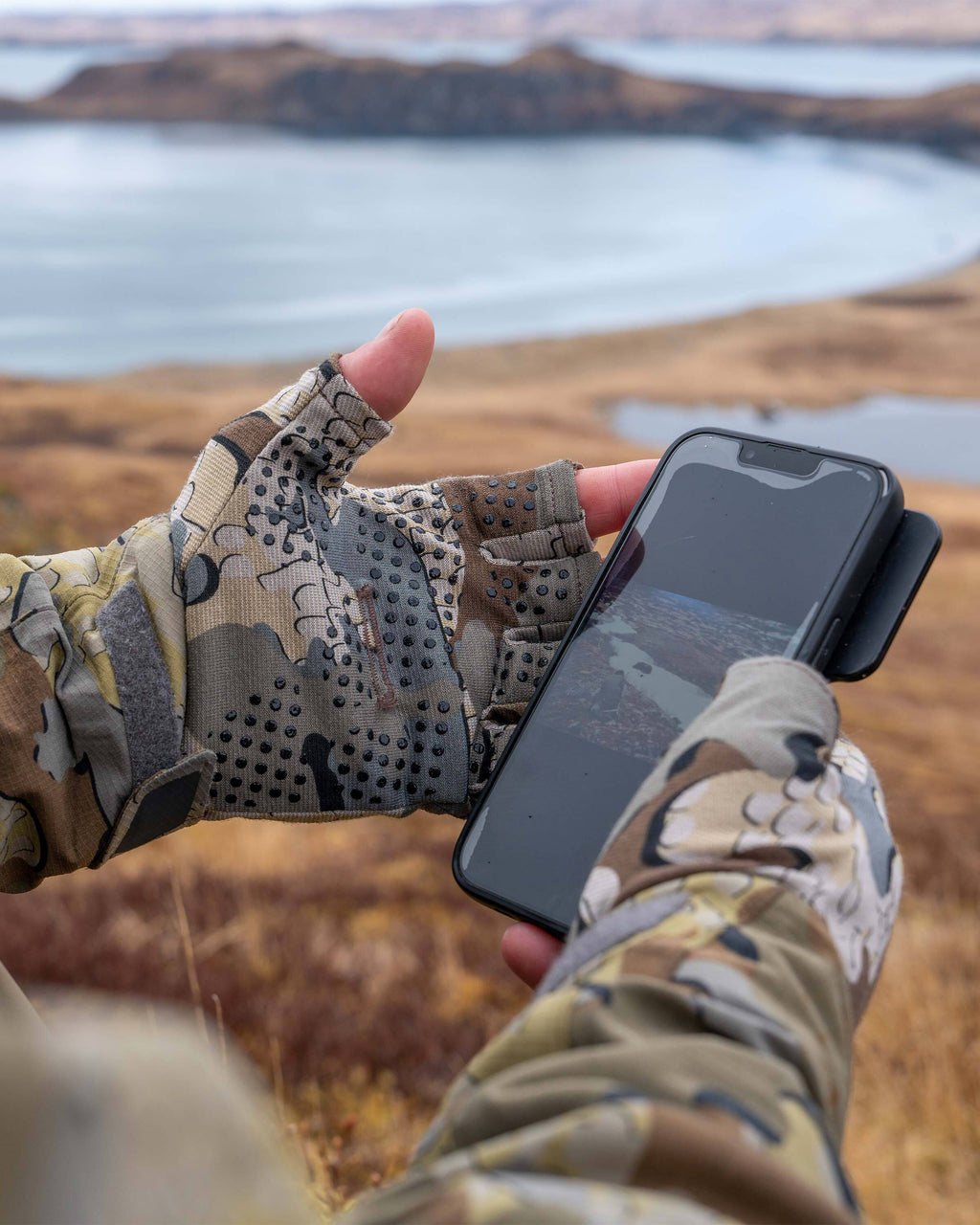Hunter holding out his cell phone, highlighting the inner palm with silicone dot matrix grip on the Ultra Merino Fingerless Glove in Valo Camouflage 