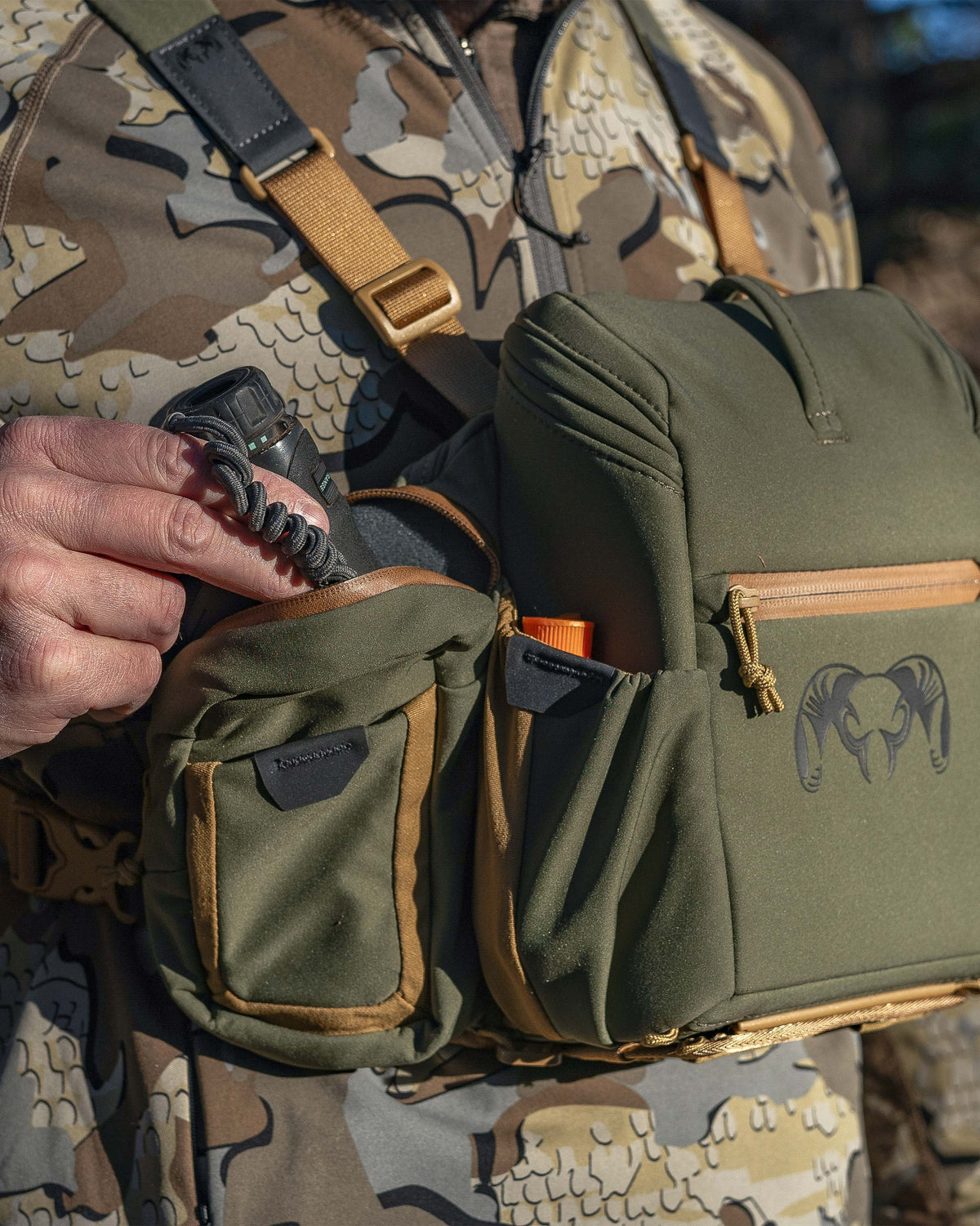 Hunter pulling out a rangefinder from right side exterior pocket of the PRO Chest Pack in Evergreen