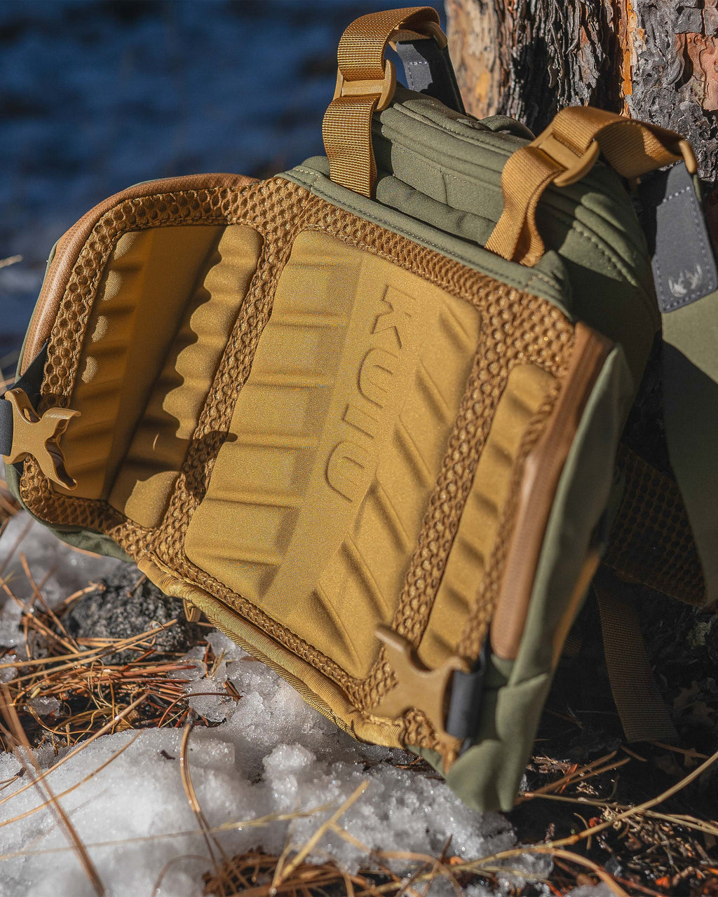 PRO Chest Pack in Evergreen leaned up against a tree on melting snow, Highlighting ergonomic and highly breathable molded foam back panel 