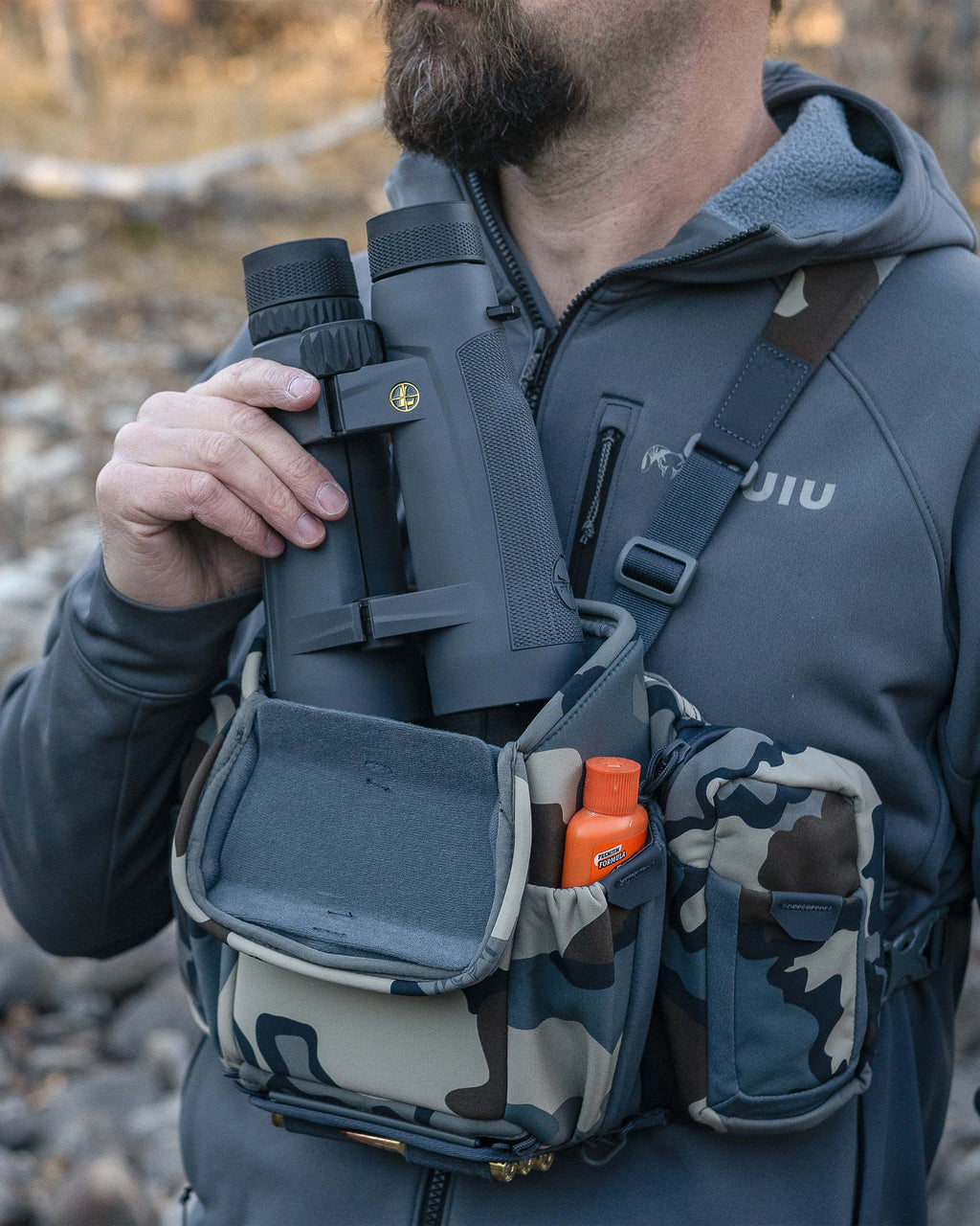 Hunter wearing the PRO Chest Pack in Vias Camouflage, pulling out a binocular from the main compartment, highlighting overlapped forward-folding lid