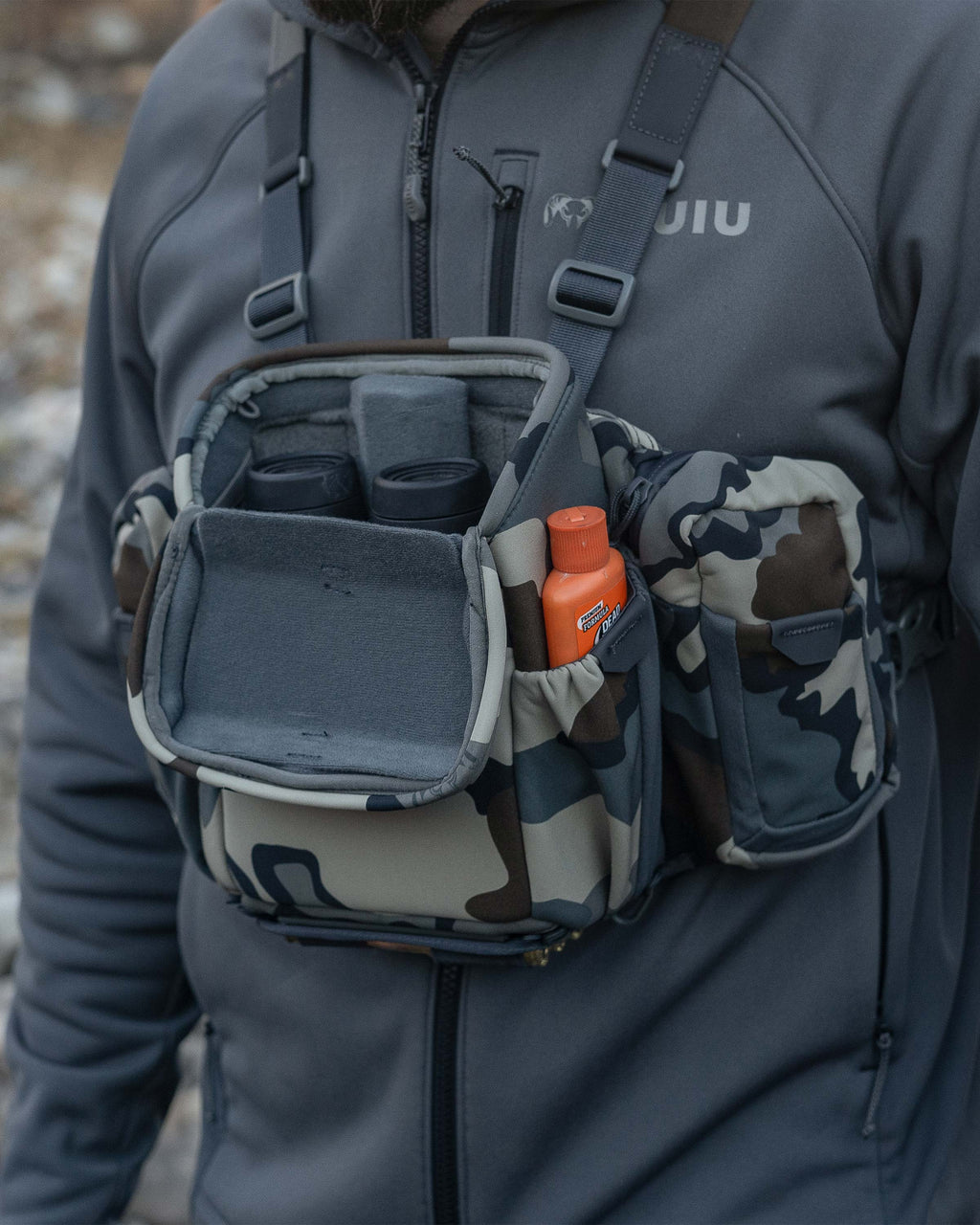 Hunter wearing the PRO Chest Pack in Vias Camouflage, Highlighting overlapped forward-folding lid and a binocular nestled inside the main compartment