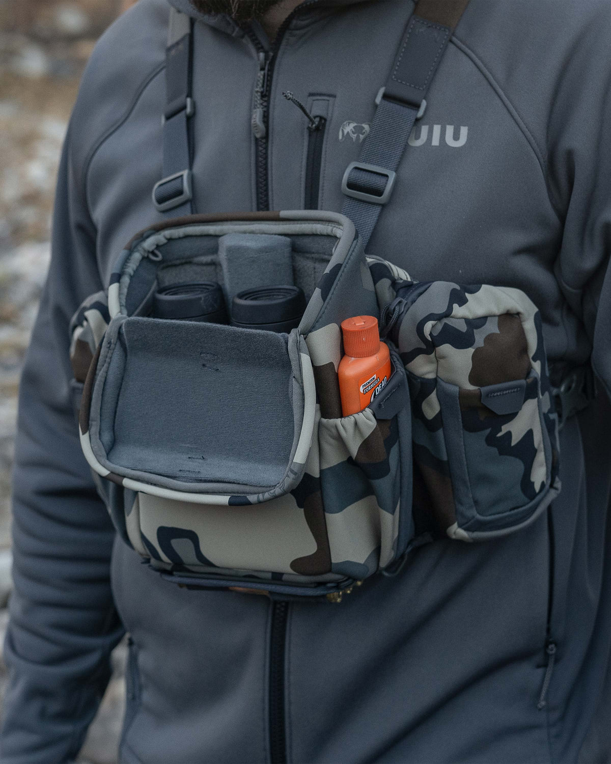 Hunter wearing the PRO Chest Pack in Vias Camouflage, Highlighting overlapped forward-folding lid and a binocular nestled inside the main compartment