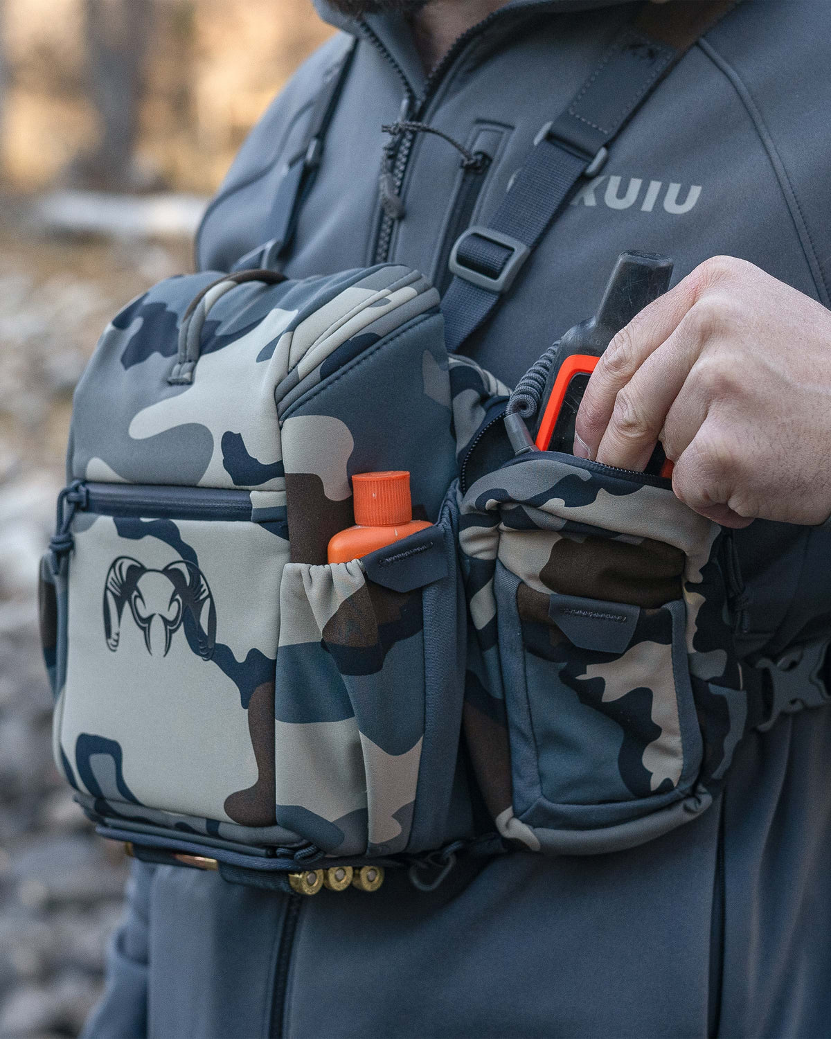 Hunter stowing an accessory item in the zip-closure side pockets on the PRO Chest Pack in Vias Camouflage