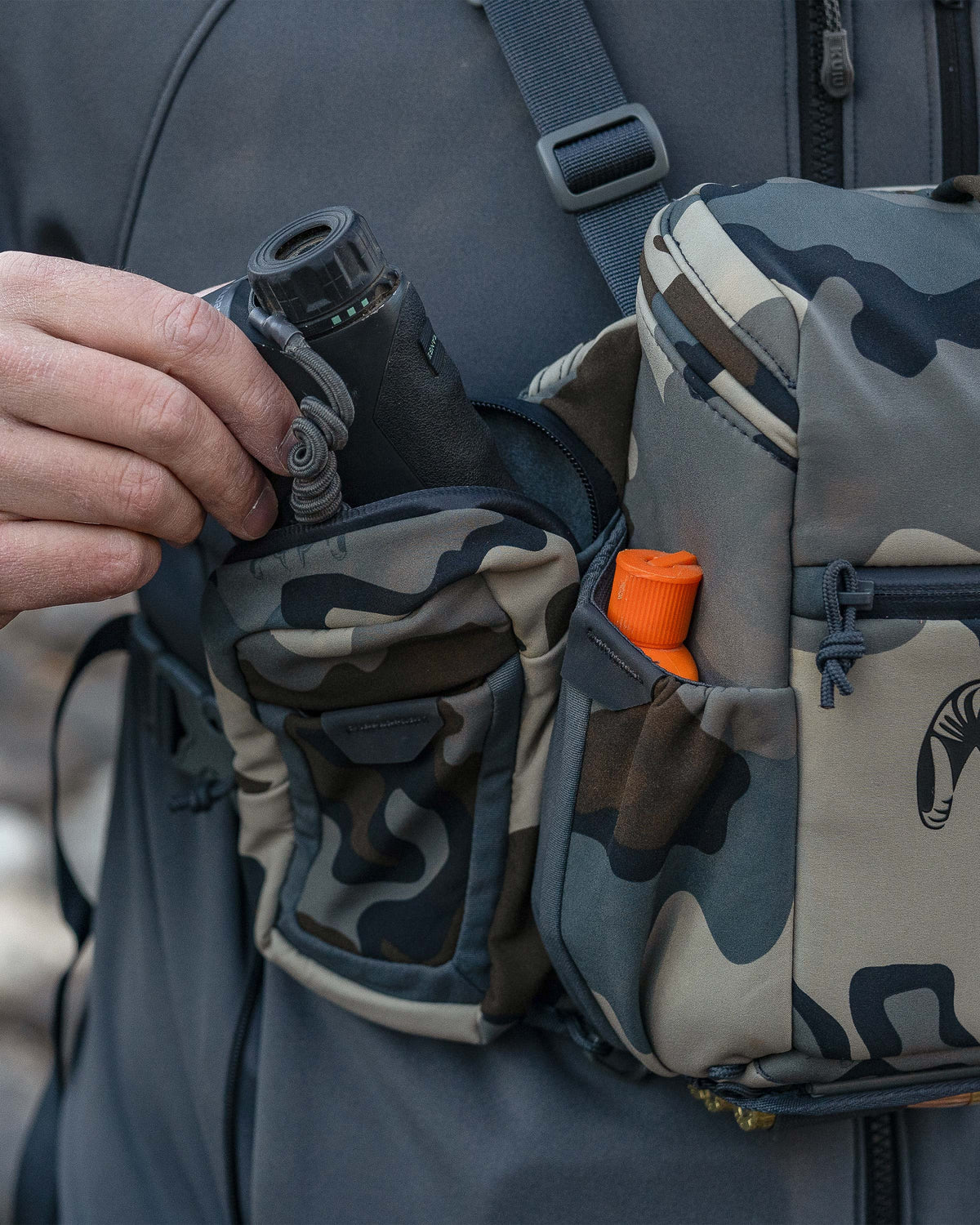 Hunter pulling out a rangefinder from right side exterior pocket of the PRO Chest Pack in Vias Camouflage