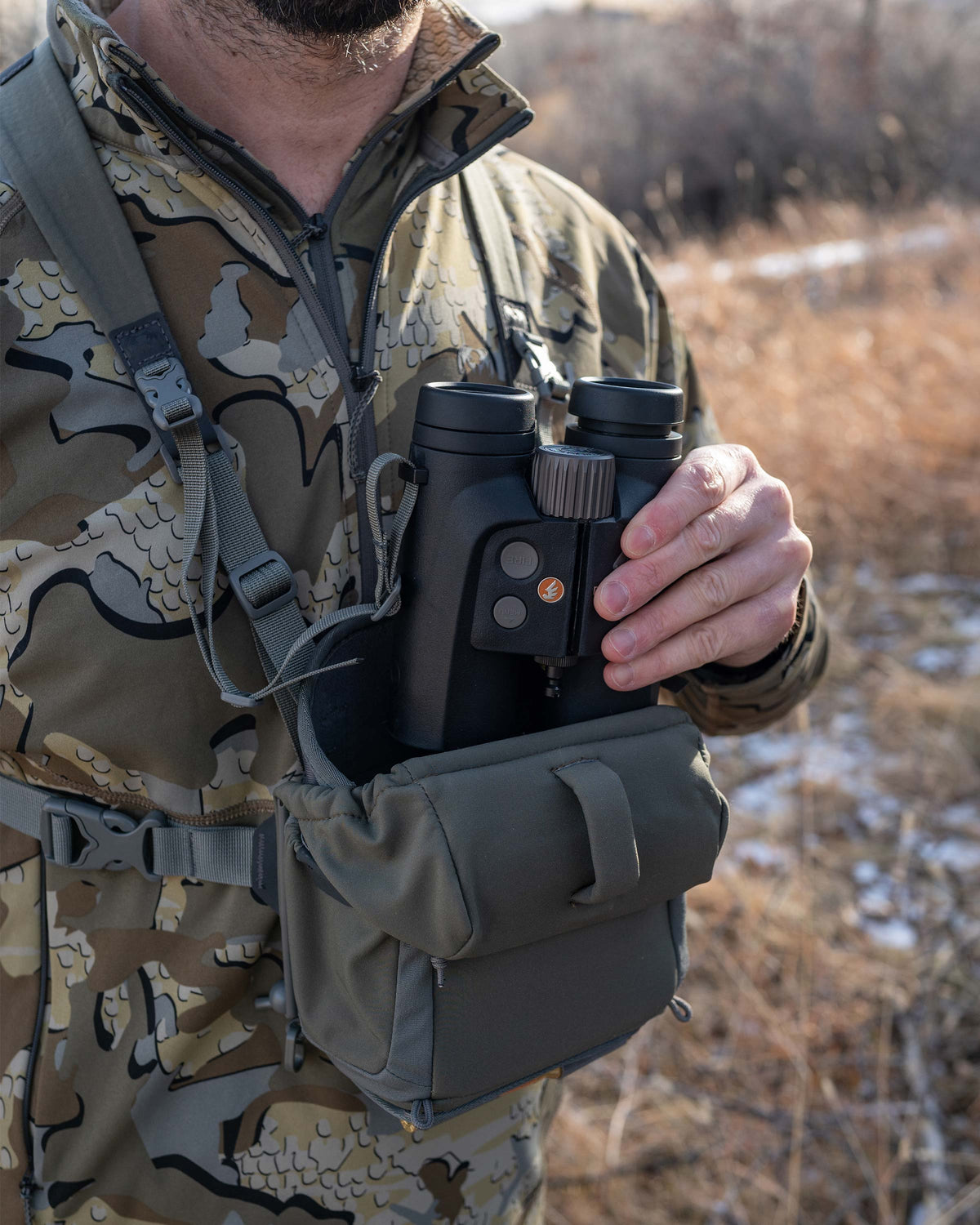 Close-up of Hunter pulling out binocular from the PRO G3 Bino Harness in Ash Brown, Highlighting opened forward-folding magnetic lid 