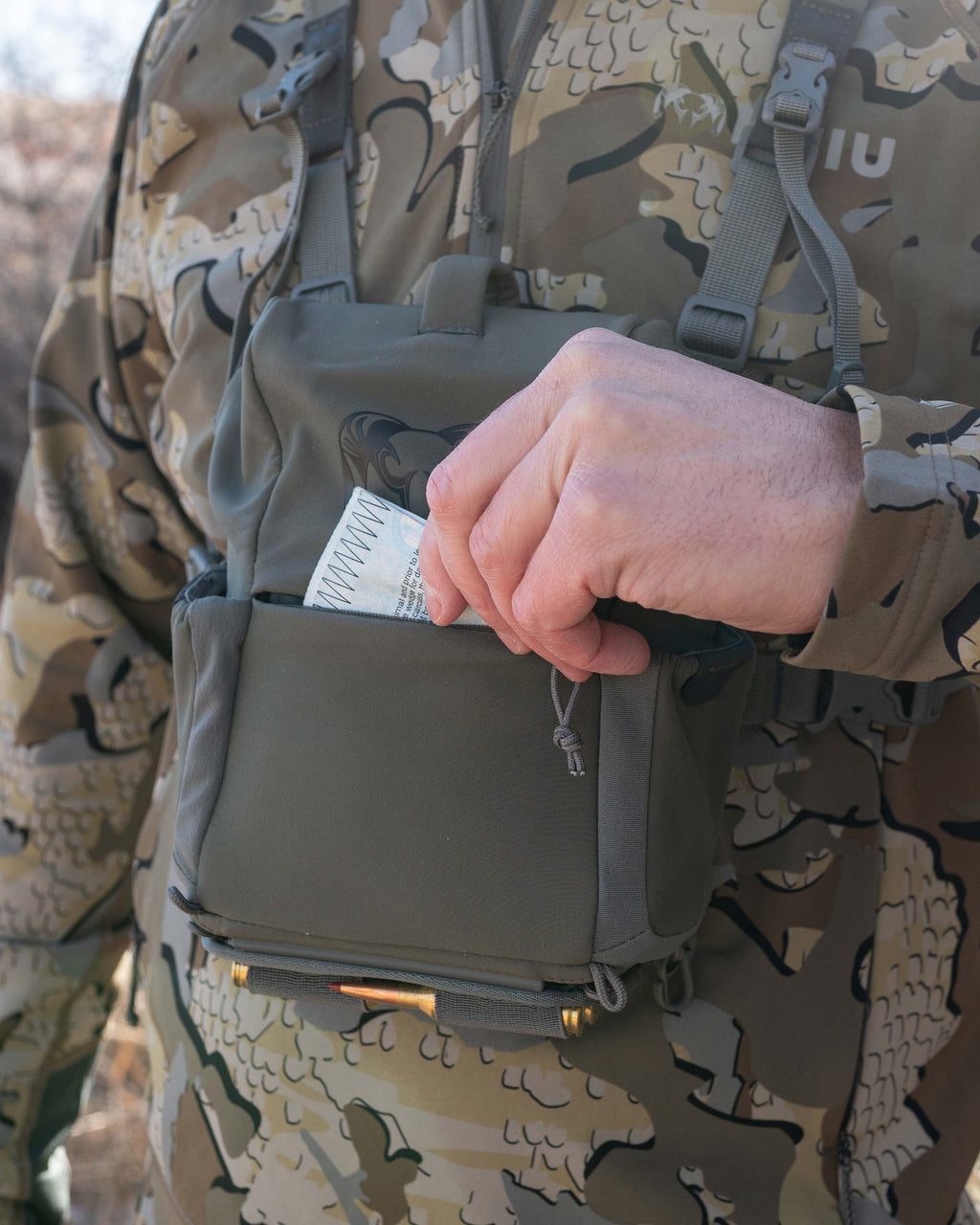 Close-up of Hunter pulling out hunting tag/license from the front zipper pocket of the PRO G3 Harness in Ash Brown