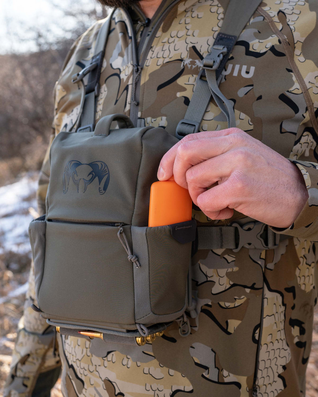 Hunter reaching for wind detector tucked inside left exterior pocket of the PRO G3 Bino Harness in Ash Brown