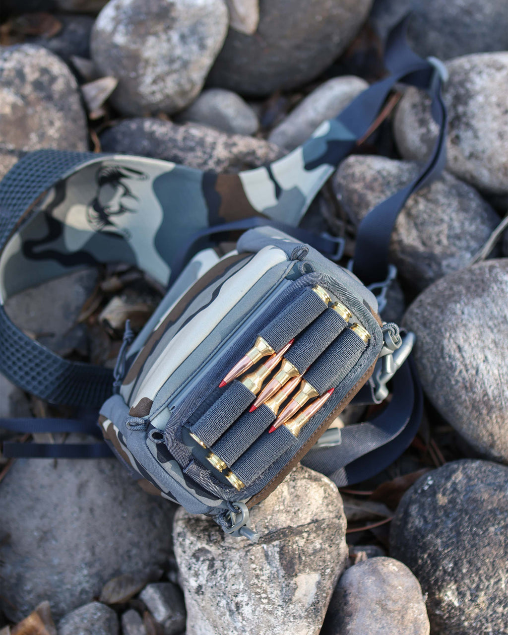 Upside down view of PRO G3 Bino Harness in Vias Camouflage on top of rocks, Highlighting bottom track system holder with ammo