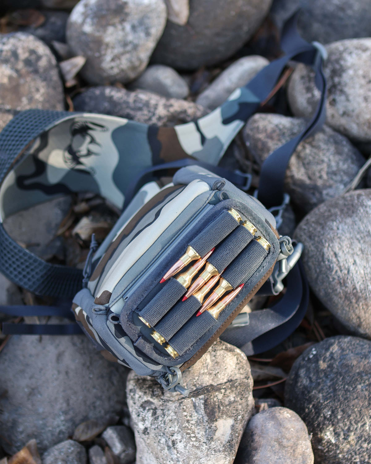 Upside down view of PRO G3 Bino Harness in Vias Camouflage on top of rocks, Highlighting bottom track system holder with ammo