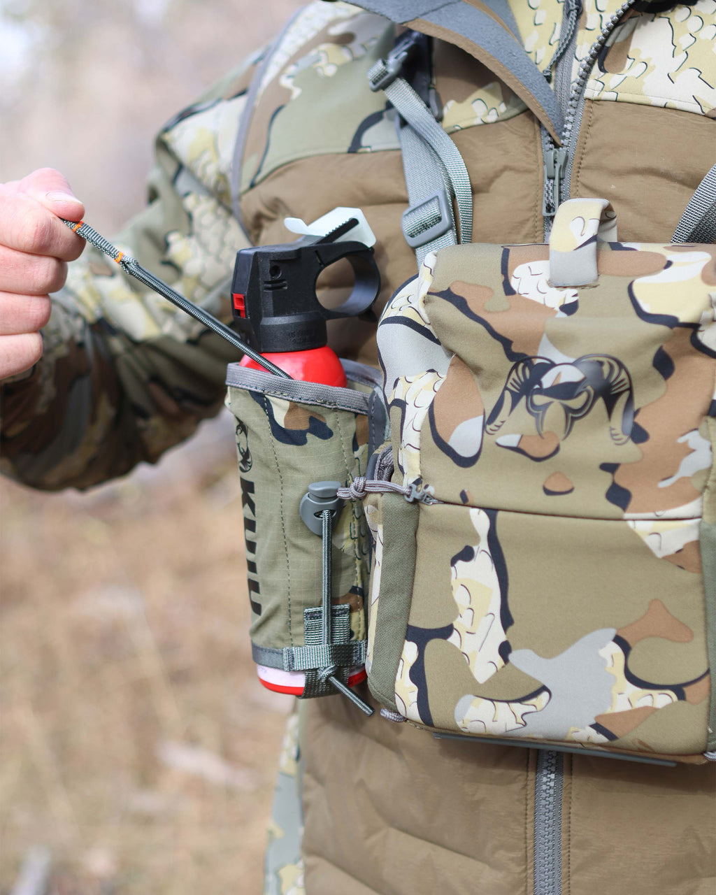 Front of Hunter wearing PRO Bino Harness with PRO G3 Bear Spray Holder in Valo Camouflage, Highlighting adjustable pull tab and cord