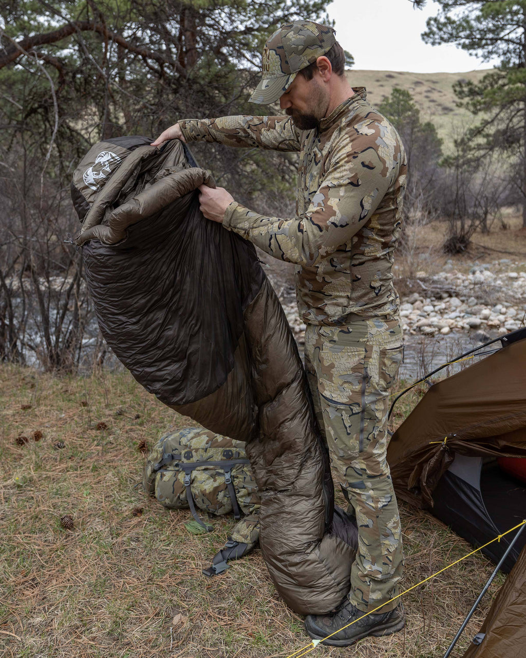 Hunter standing up to shake out Super Down Altai 0 degree sleeping bag in Ash Brown after removing it from the compression sack