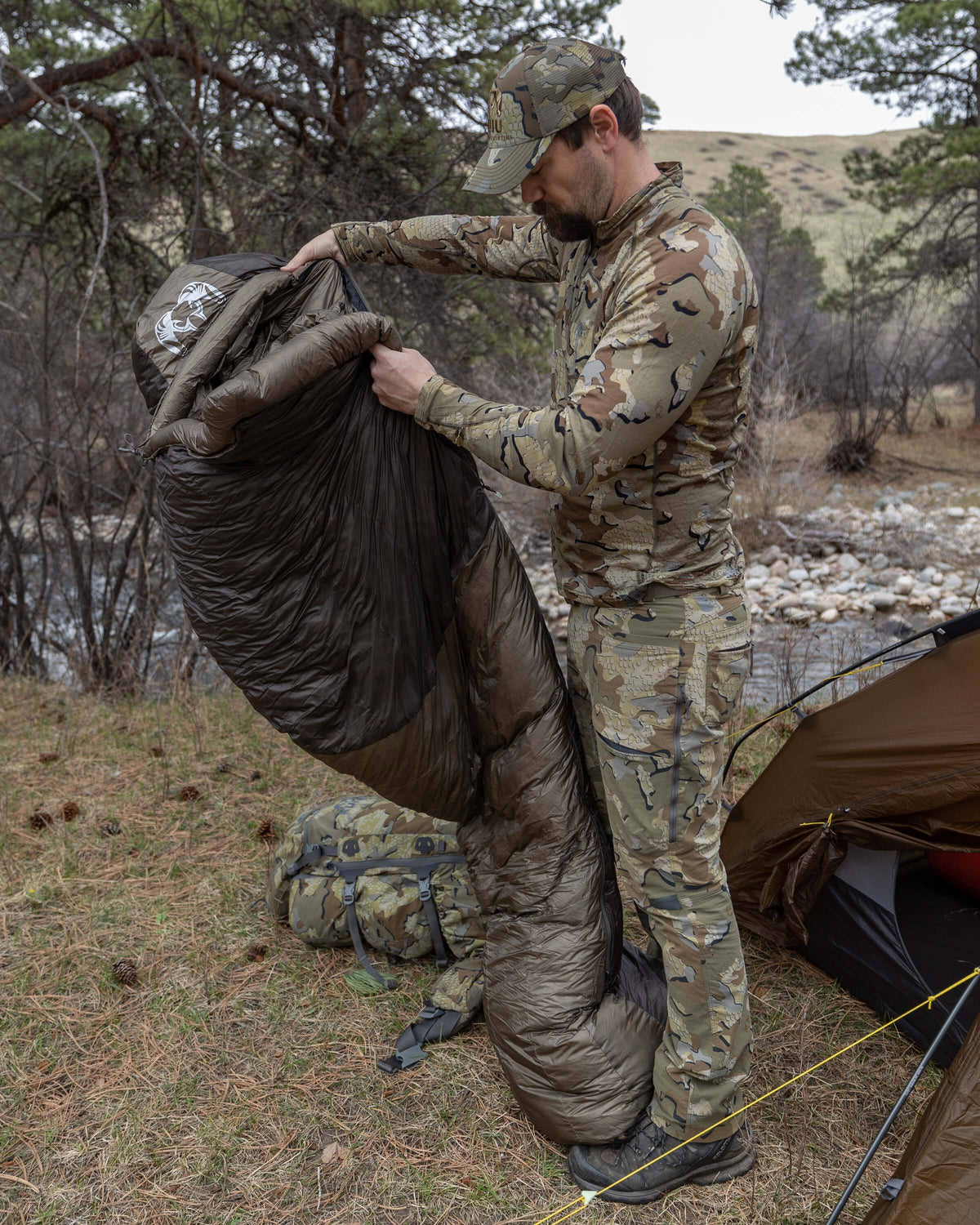 Hunter standing up to shake out Super Down Altai 0 degree sleeping bag in Ash Brown after removing it from the compression sack