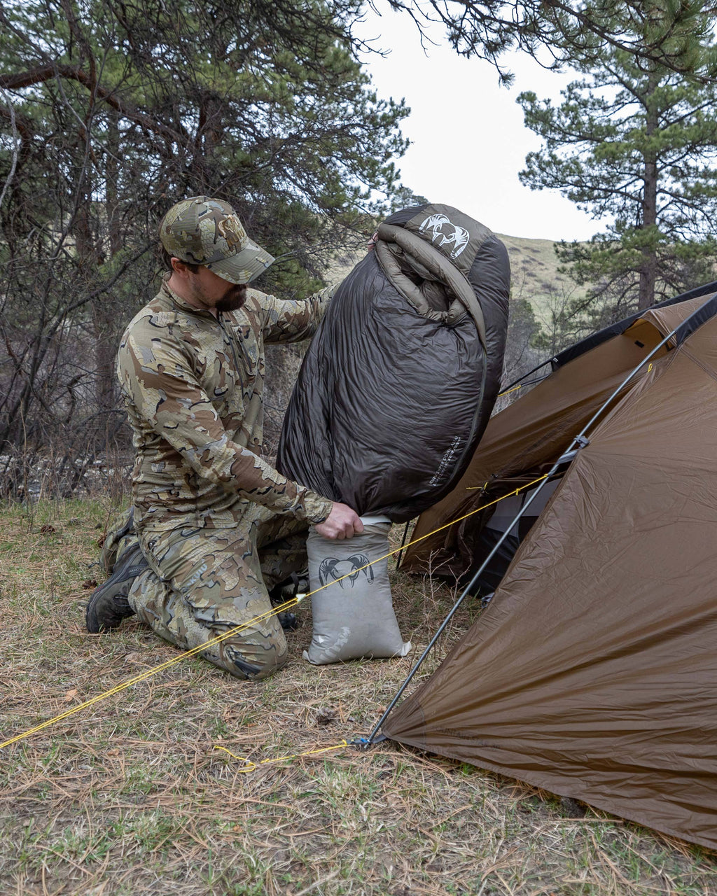 Hunter kneeling to remove the Super Down Altai 15 degree sleeping bag in Gunmetal Grey from a clear roll top dry bag