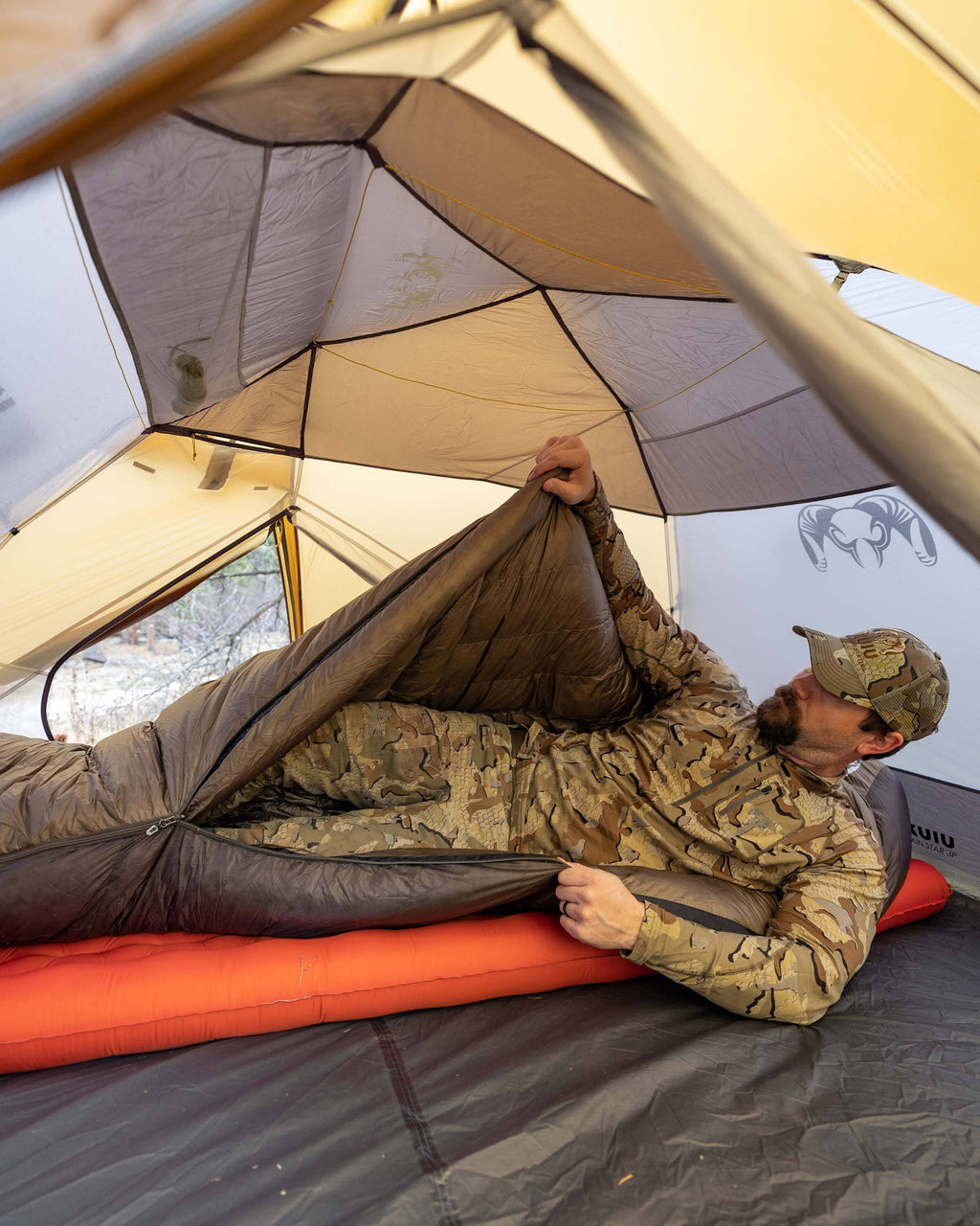 Hunter climbing into his Super Down Altai 0 degree sleeping bag in Ash Brown laid inside of his Mountain Star 3 Person Tent in preparation for sleep
