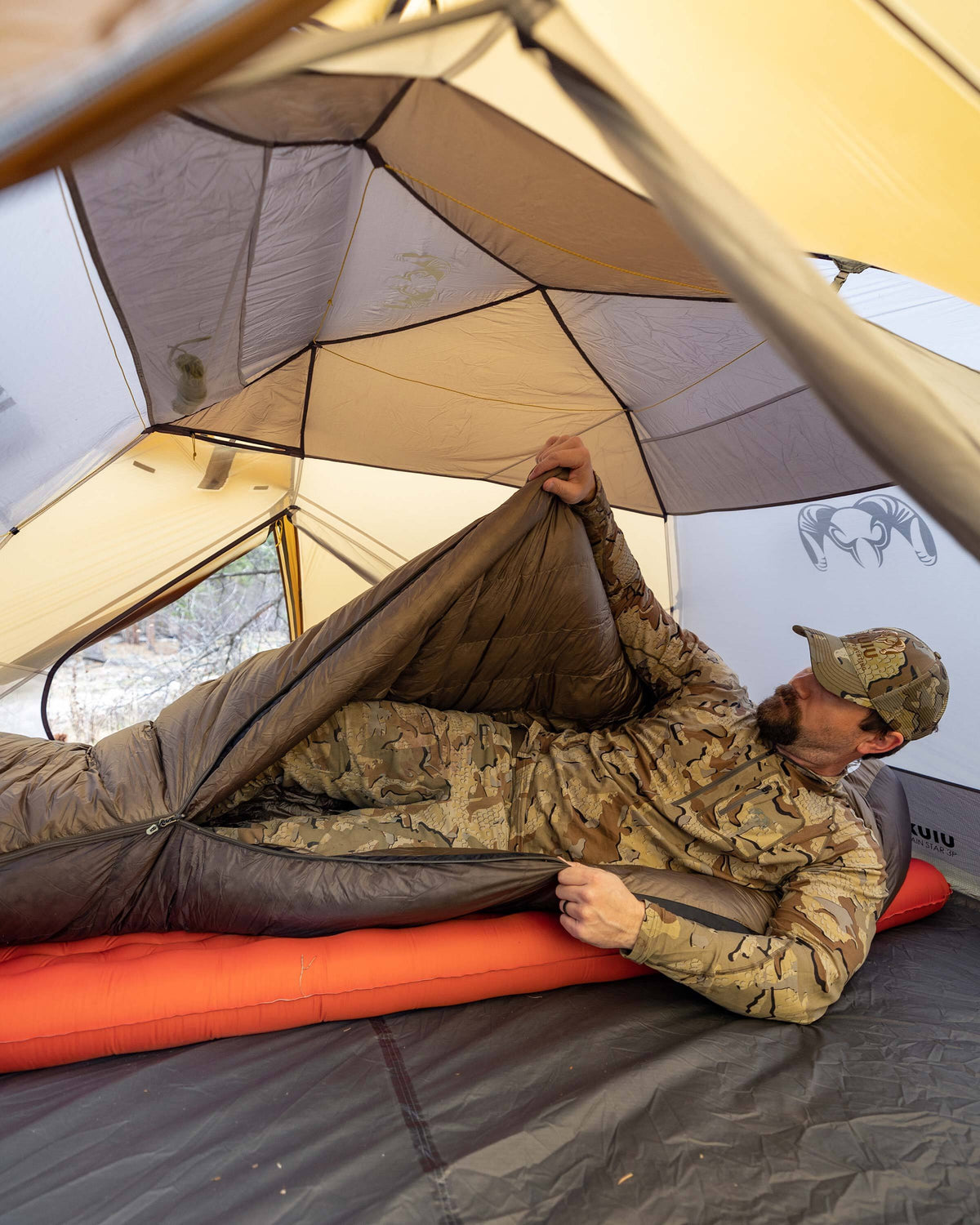 Hunter climbing into his Super Down Altai 0 degree sleeping bag in Ash Brown laid inside of his Mountain Star 3 Person Tent in preparation for sleep