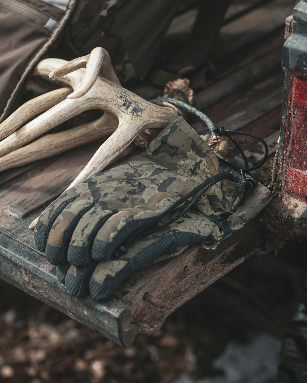 A pair of Northstar Glove in Veros camouflage hunting gloves, resting on a rustic wooden surface next to natural deer antlers.