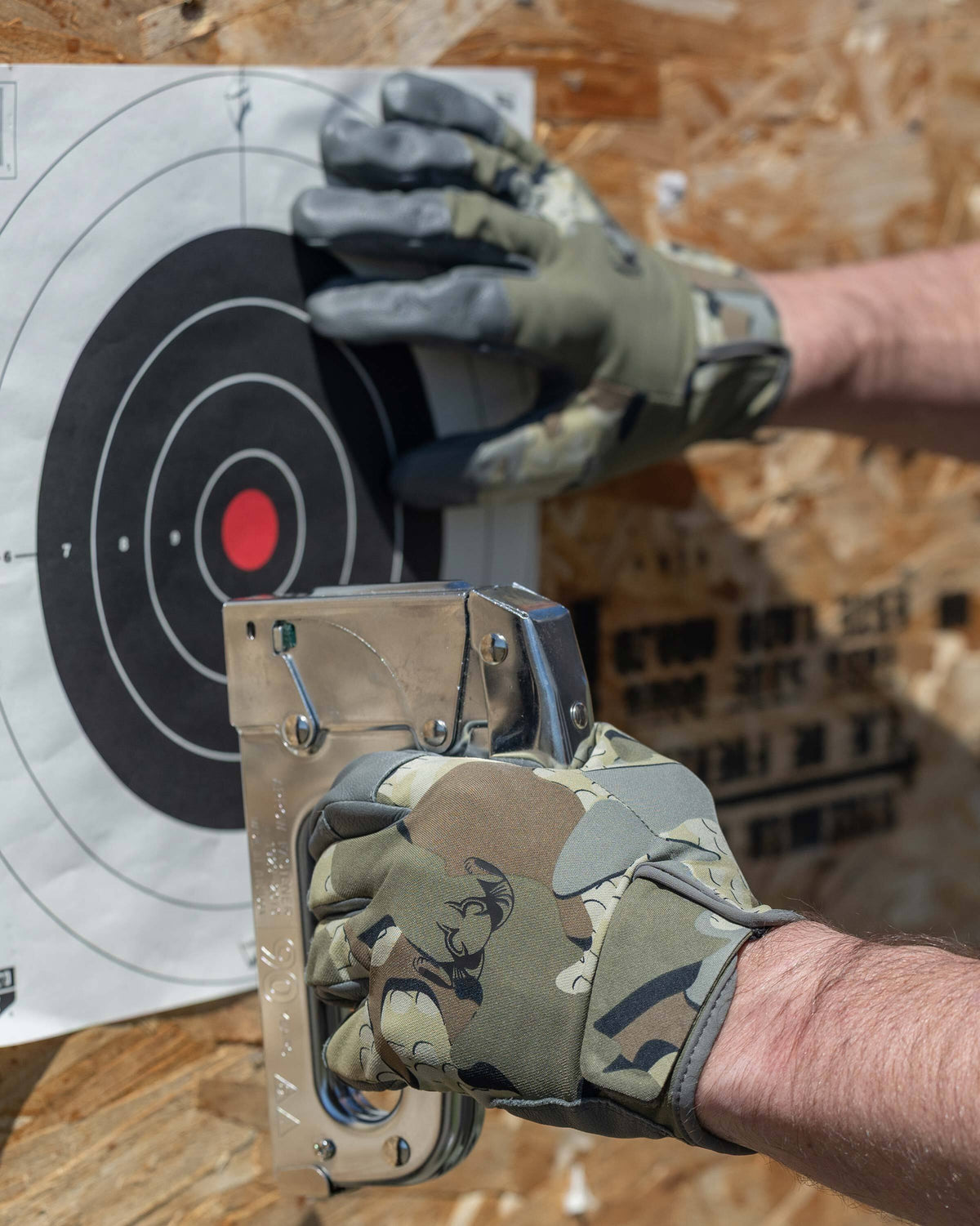 Hunter wearing Precision Glove in Valo Camouflage stapling paper target on a wood back board