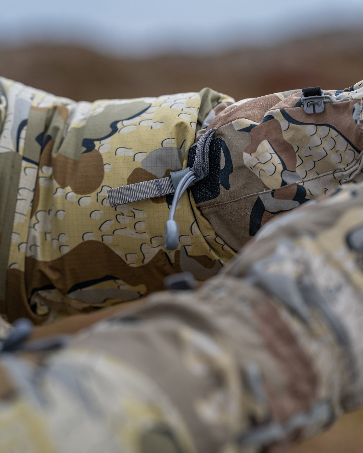 Close-up of Yukon Hardshell Glove in Valo camouflage with a gray drawcord at the wrist, worn outdoors with a blurred natural background.