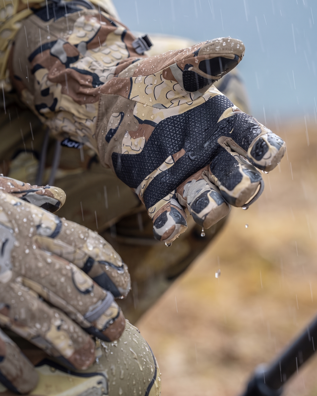 Close-up of a hunter in the rain wearing Yukon Hardshell Glove in Valo camouflage showing the inner palm and grip texture.
