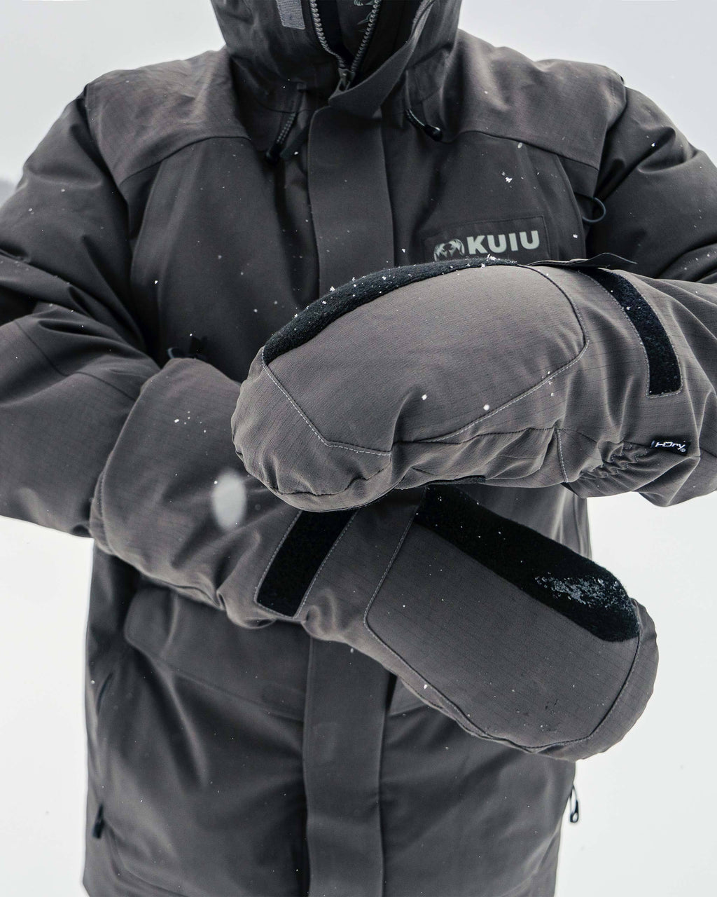 Front of hunter in a snowy outdoor environment, strapping on Super Down Arktuk Down Mitt in Asphalt Grey