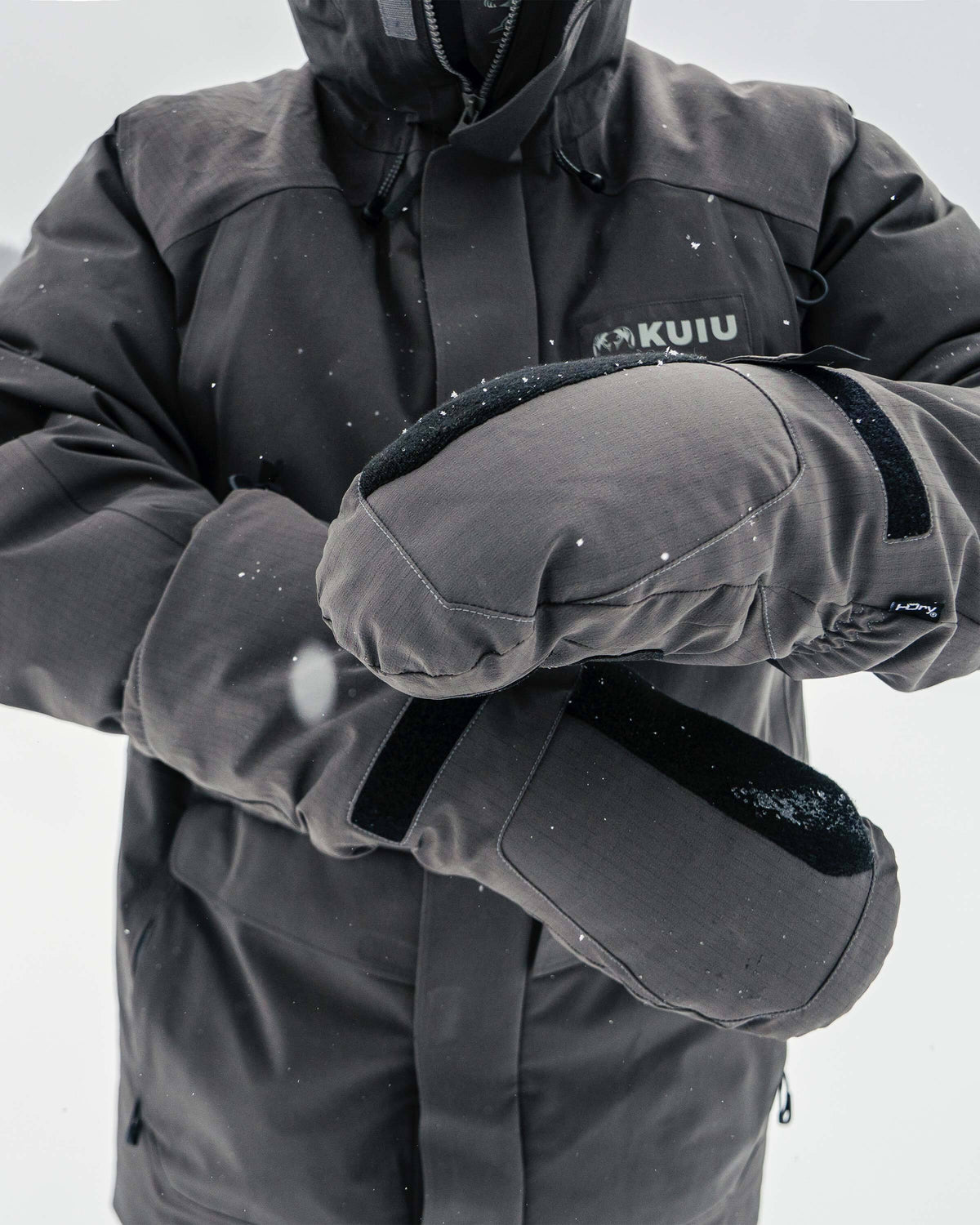 Front of hunter in a snowy outdoor environment, strapping on Super Down Arktuk Down Mitt in Asphalt Grey