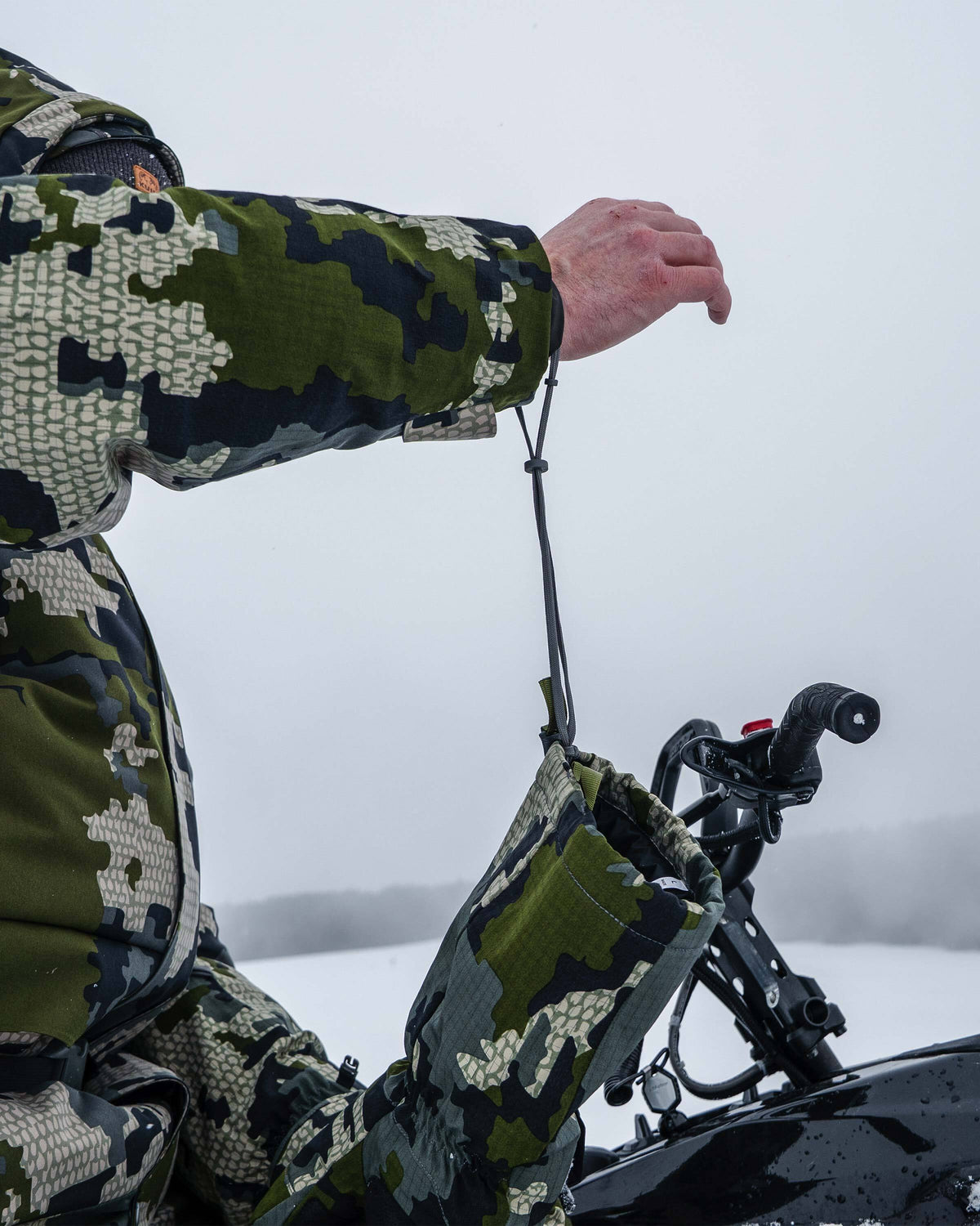 Hunter demonstrating the removable wrist leash that secures the Super Down Arktuk Mitt in Verde Camouflage