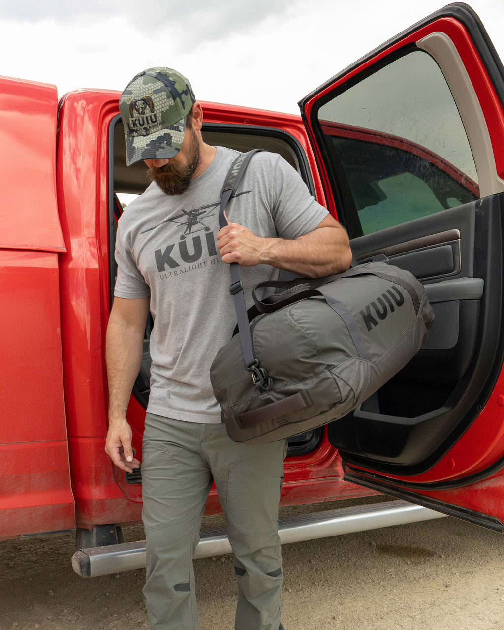 Man walking away from a red truck, carrying Runway CORDURA® 3000 Duffel Asphalt Grey on his left shoulder