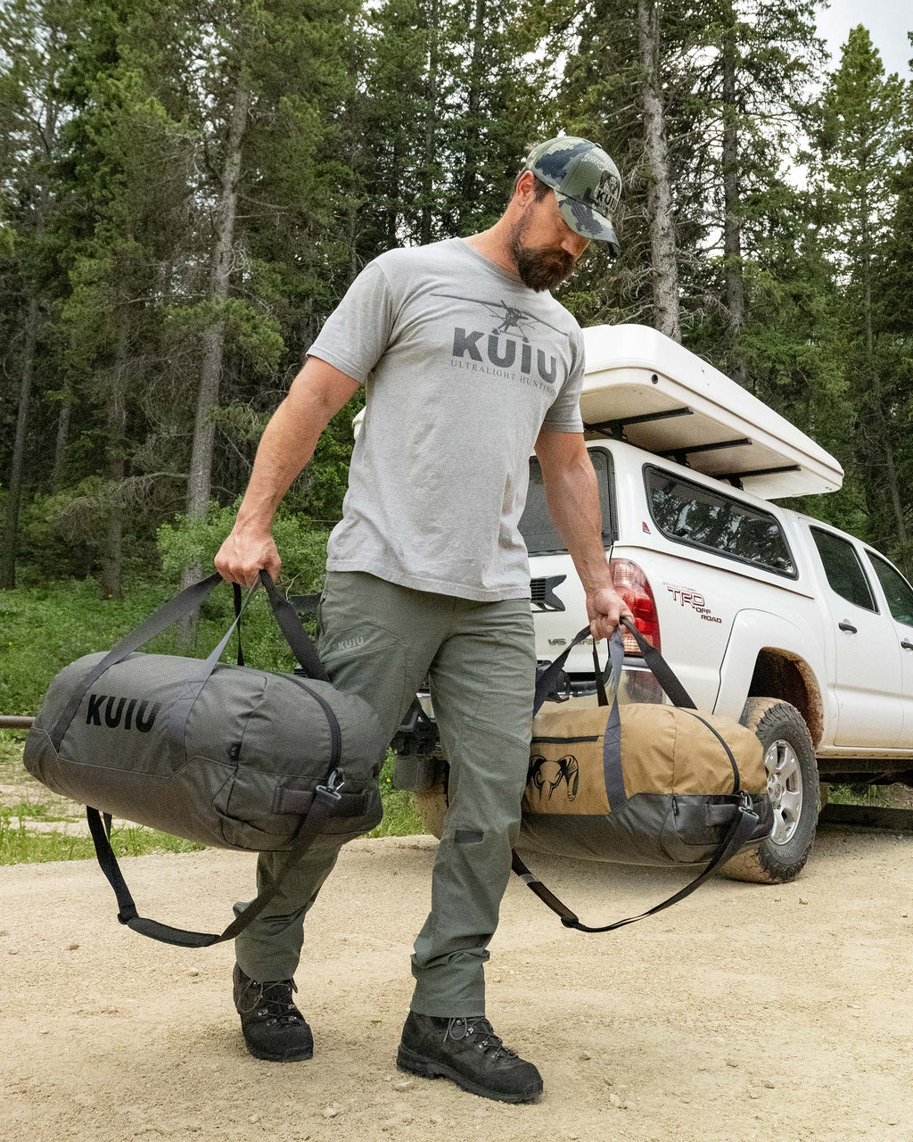 Man in an forrest setting carrying a Asphalt Grey and Coyote Brown Runway CORDURA® Duffel one in each hand