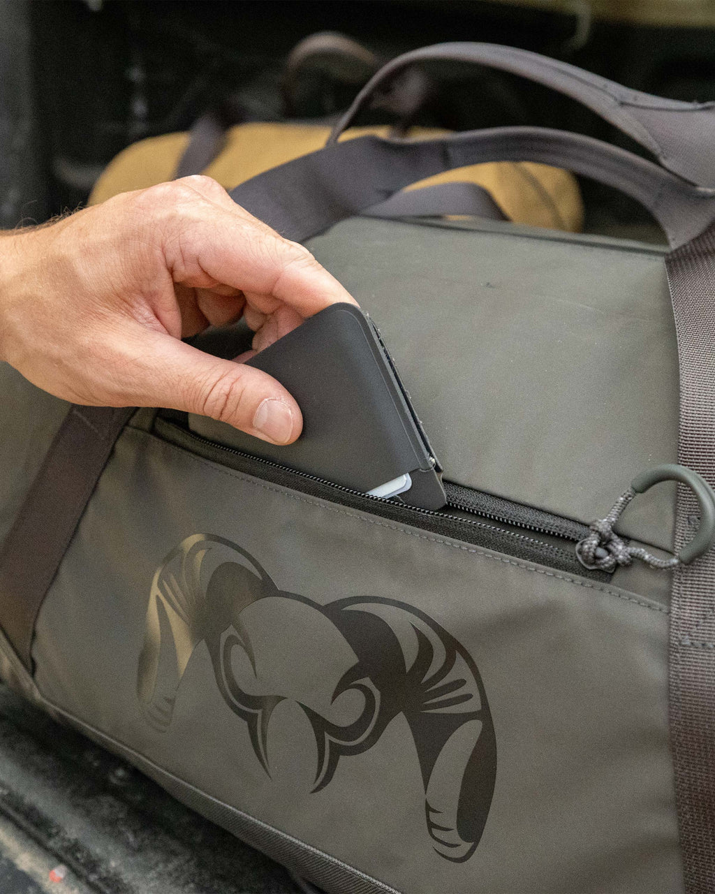 Close-up of man stowing a wallet in the outer zippered pocket of the Runway CORDURA® Duffel in Asphalt Grey