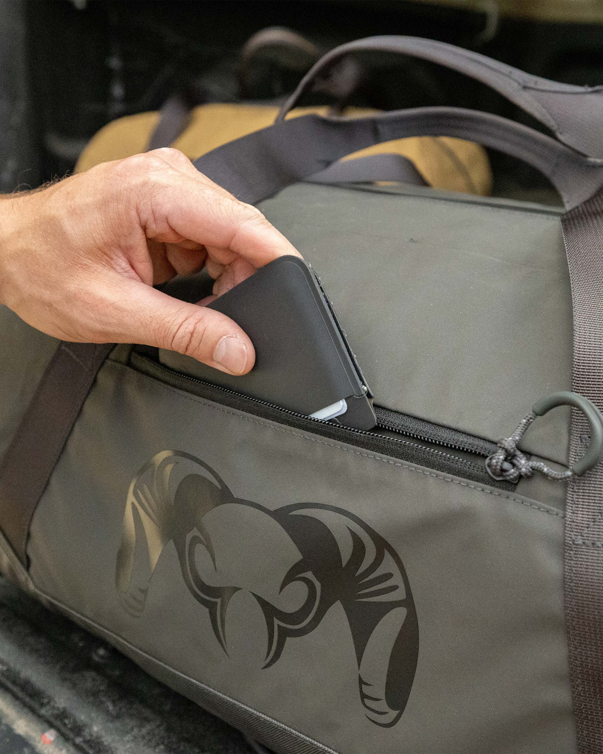 Close-up of man stowing a wallet in the outer zippered pocket of the Runway CORDURA® Duffel in Asphalt Grey