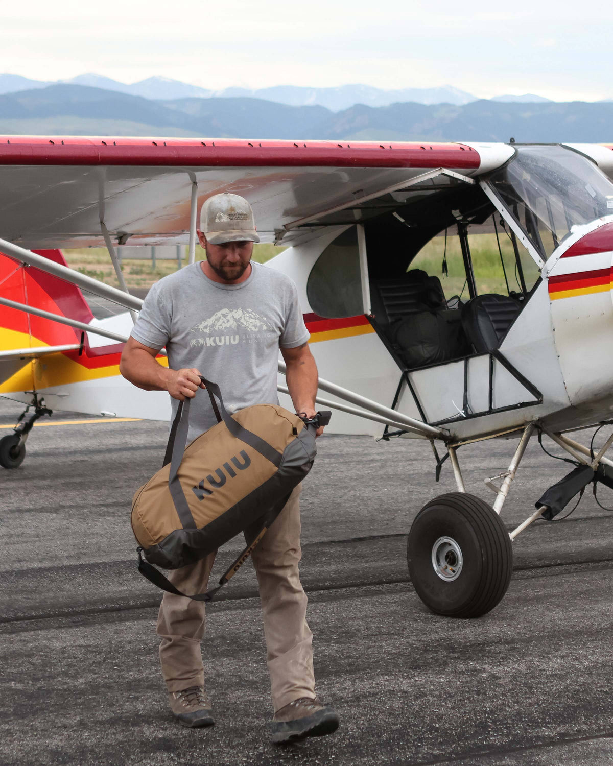 Man walking away from a Super Cub plane carrying a Runway CORDURA® Duffel in Coyote Brown