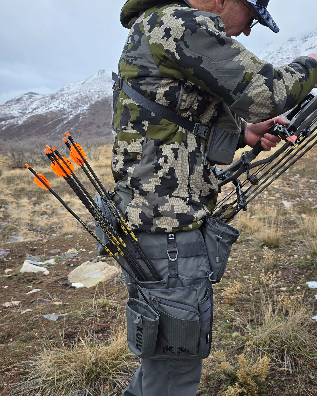 Archery Hip Quiver in Gunmetal Attached to Mans right leg, side angle shot zoomed out to show arrows and Man working on the bow