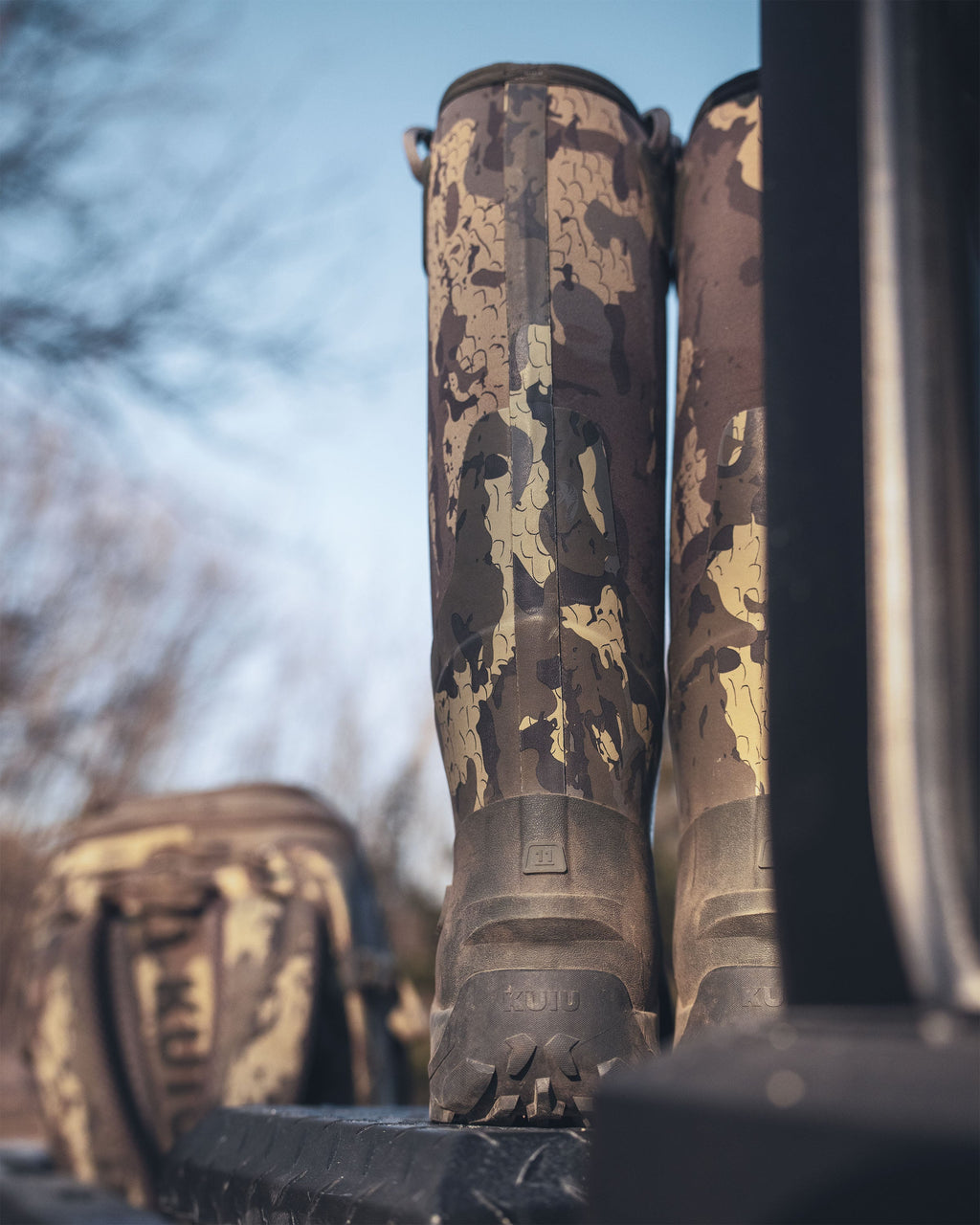 Back view of KUIU Mud boots in Veros camouflage rest on the edge of a pickup truck tailgate.