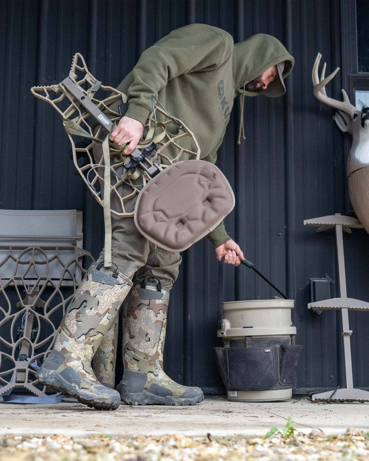 Hunter leaning forward, picking up a bucket, wearing KUIU Mud Boot in Valo Camouflage