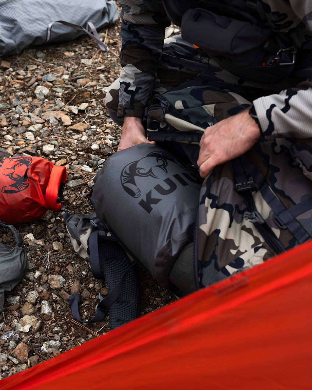 Hunter loading the filled Stone Grey HD Roll Top Dry Bag into the main compartment of his pack