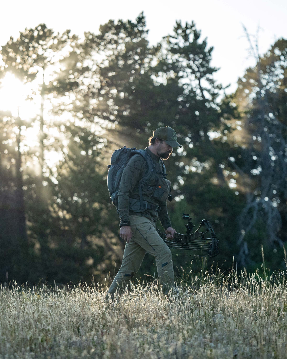 Hunter backpacking through the meadow carrying his bow, wearing Ridgepoint Fleece Henley in Olive Green Tonal Pattern