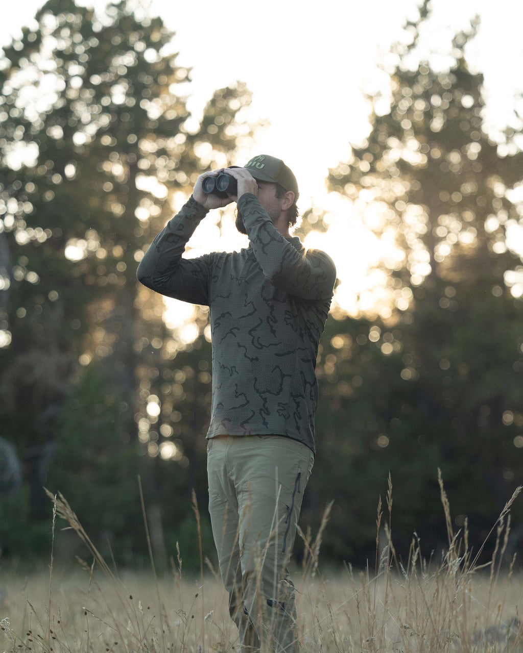 Hunter standing in the meadow, looking through a binocular, wearing Ridgepoint Fleece Henley in Olive Green Tonal Pattern