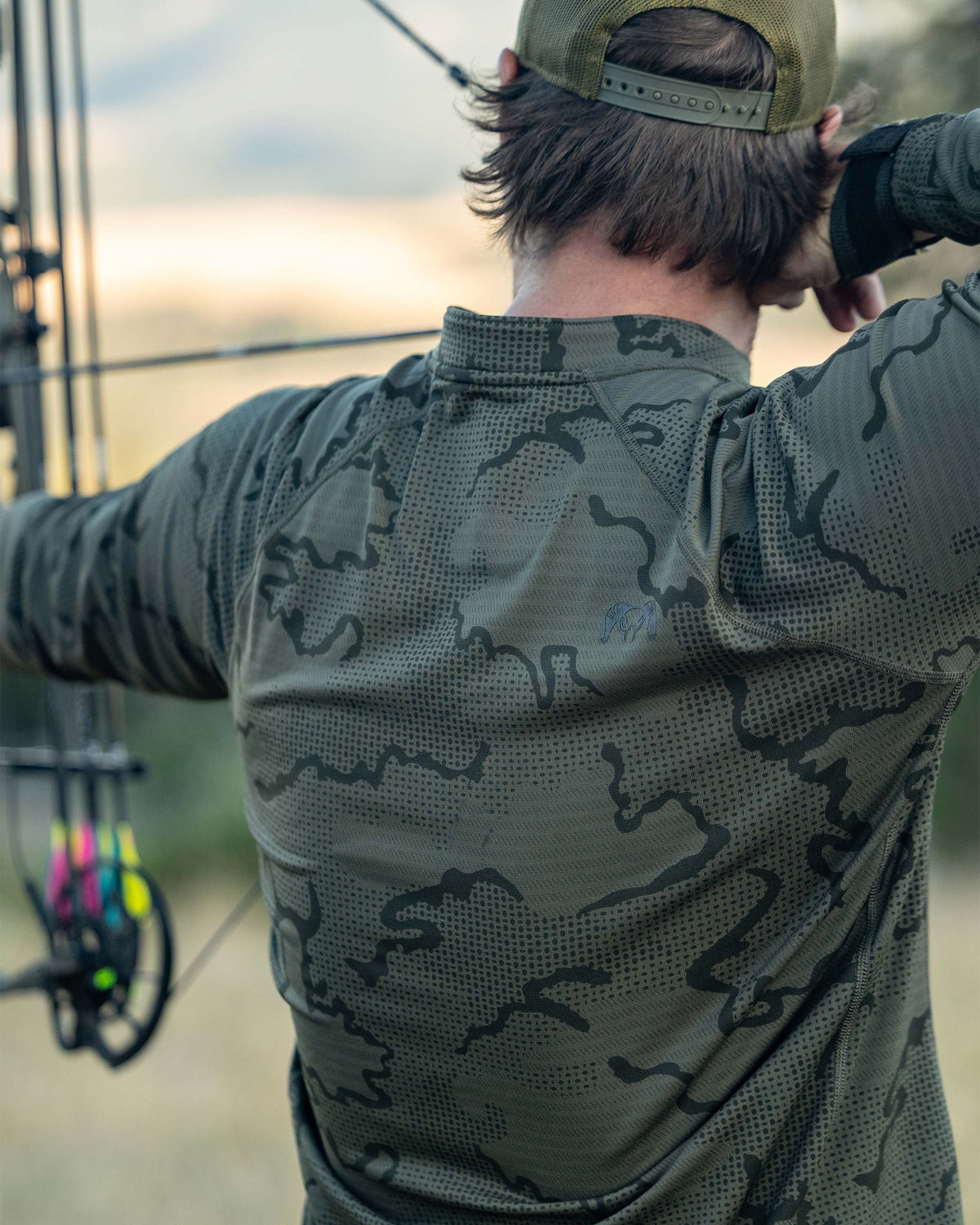 Back view of Hunter shooting a bow and arrow, wearing Ridgepoint Fleece Henley in Olive Green Tonal Pattern