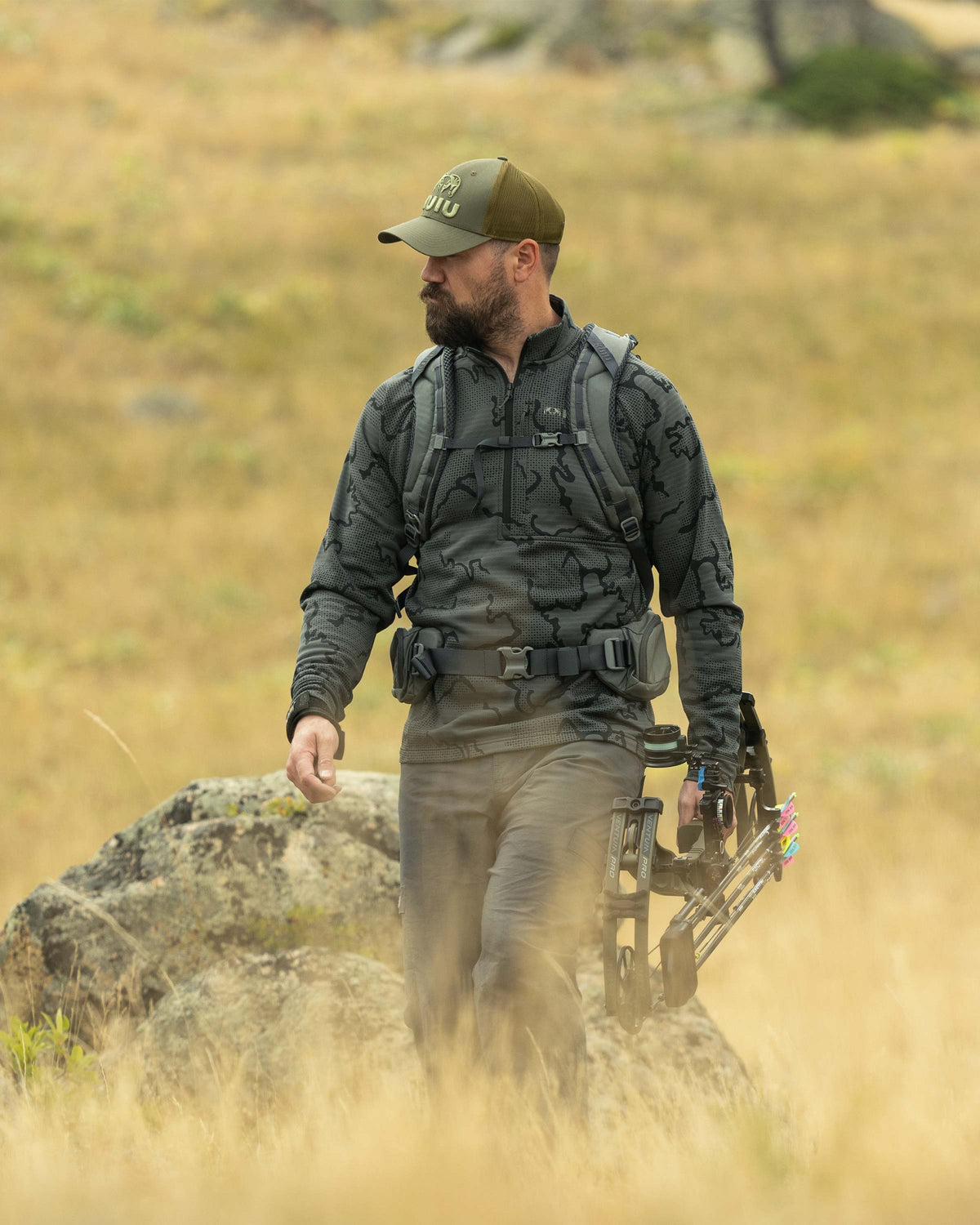 Hunter backpacking down a hill holding a bow and arrow, wearing Ridgepoint Fleece Zip-T in Olive Green Tonal Pattern 