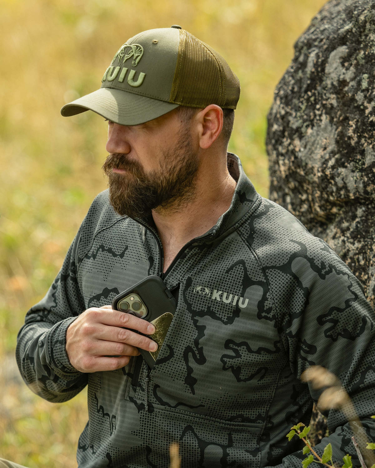Hunter slipping a cellphone in his left chest pocket, wearing Ridgepoint Fleece Zip-T in Olive Green Tonal Pattern 