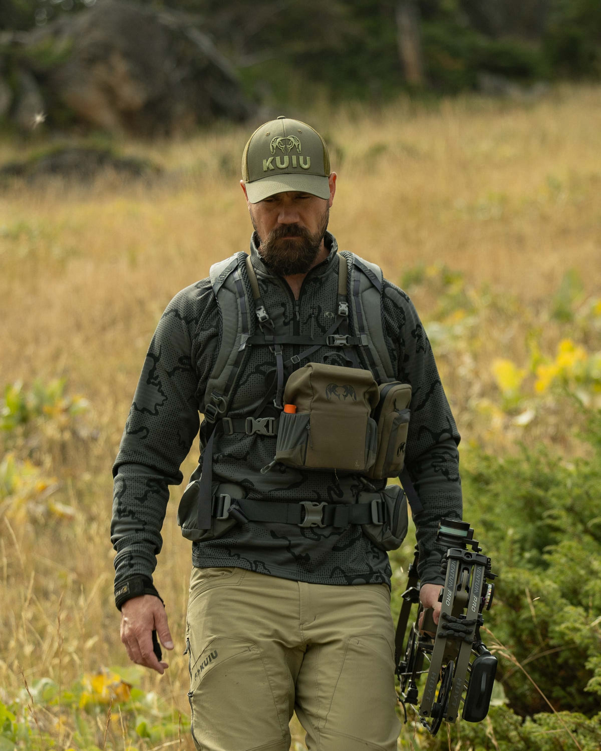 Hunter backpacking down the hill, holding his bow and arrow, wearing Ridgepoint Fleece Zip-T in Olive Green Tonal Pattern 