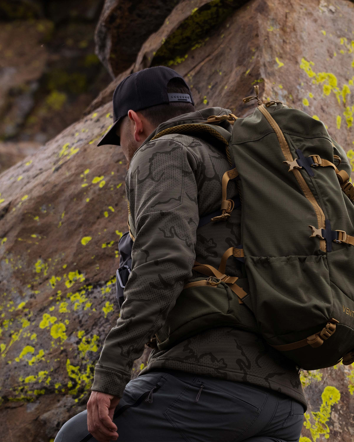 Hunter backpacking, hiking up along a rocky mountain terrain, wearing Ridgepoint Fleece Hoodie in Ash Tonal Brown